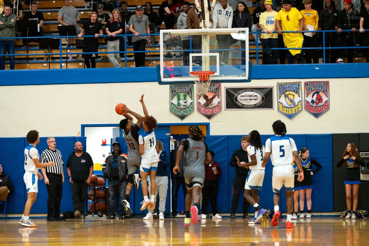 High school basketball players contest shot near basket in packed gymnasium.