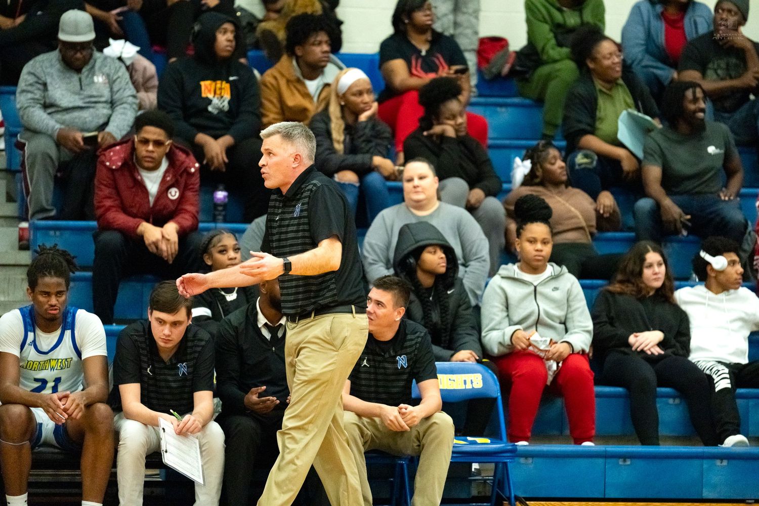 Northwest high school basketball coach gestures with clipboard on sideline during an intense game.