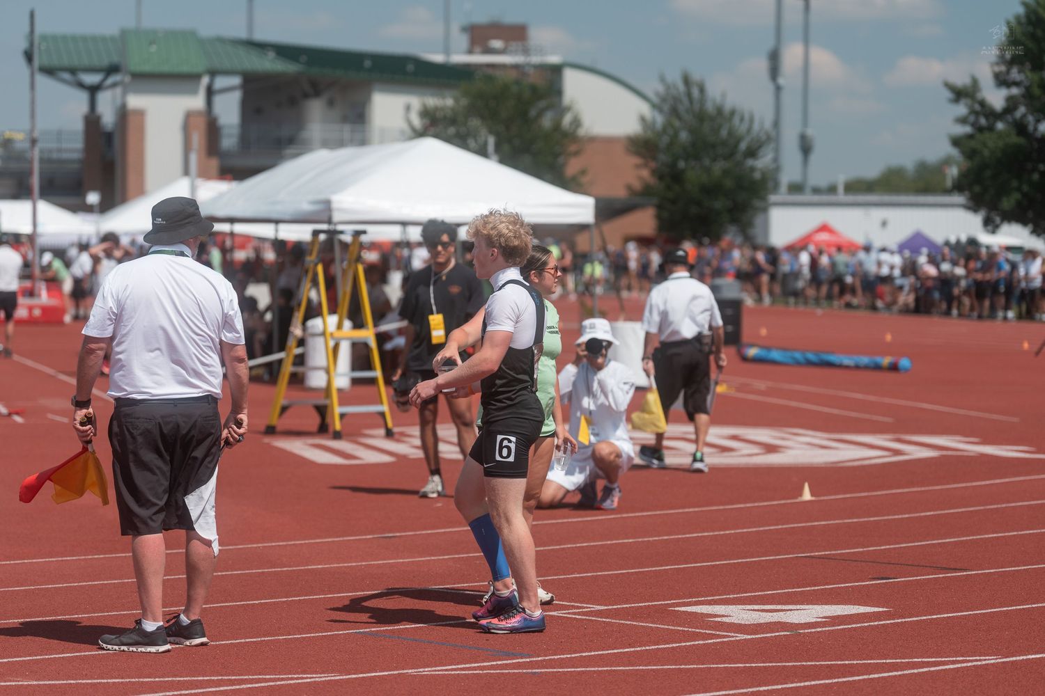 Female track athlete walks on a red outdoor track during a sunny track and field competition.