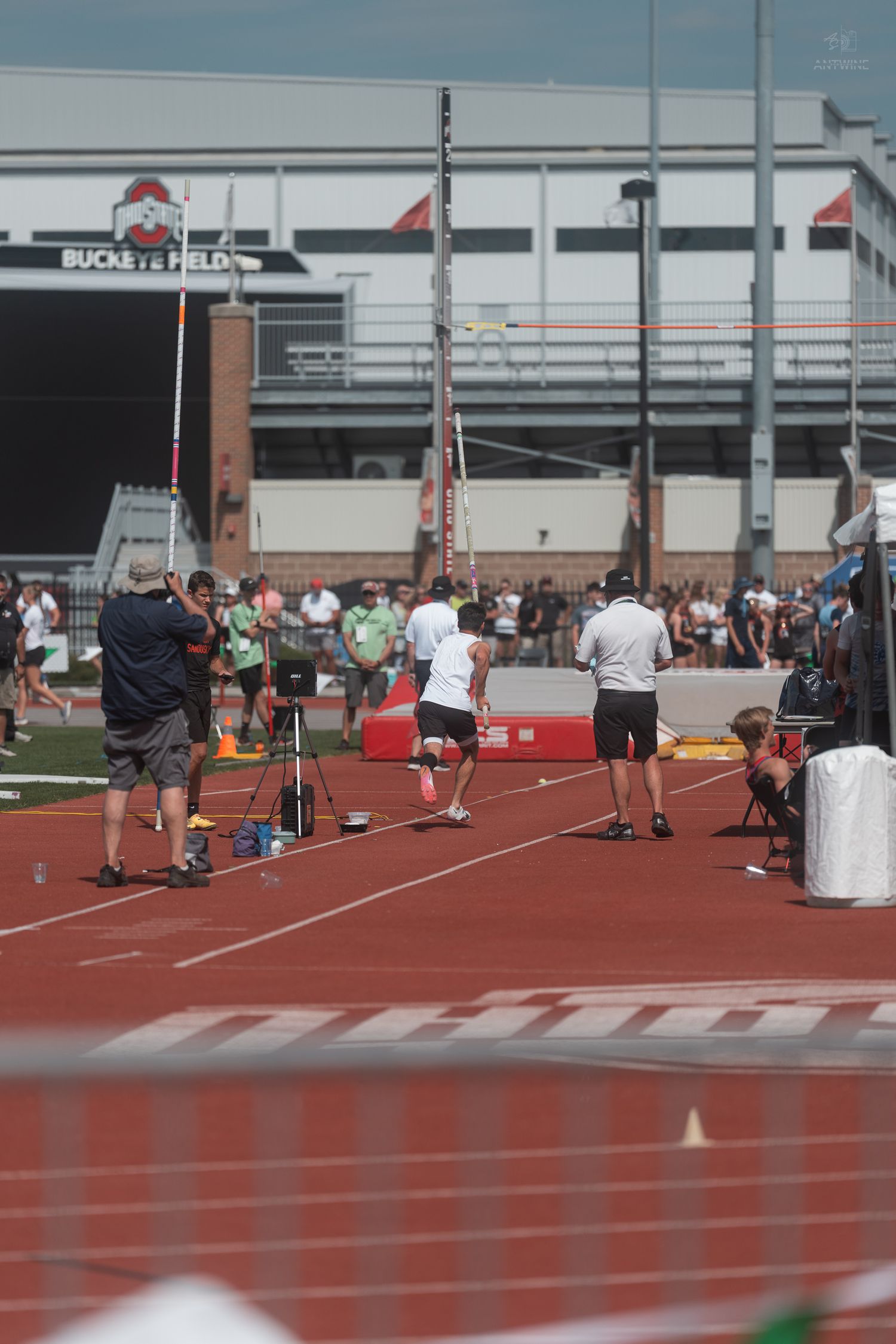 Pole vault competition at Buckeye Field with athletes and officials on a red track.