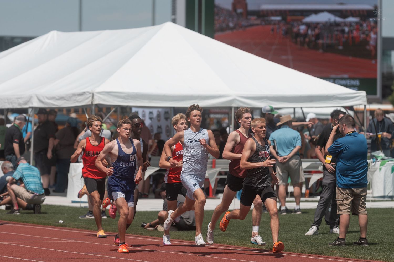 Group of male athletes running a middle distance race at an outdoor track and field championship event.