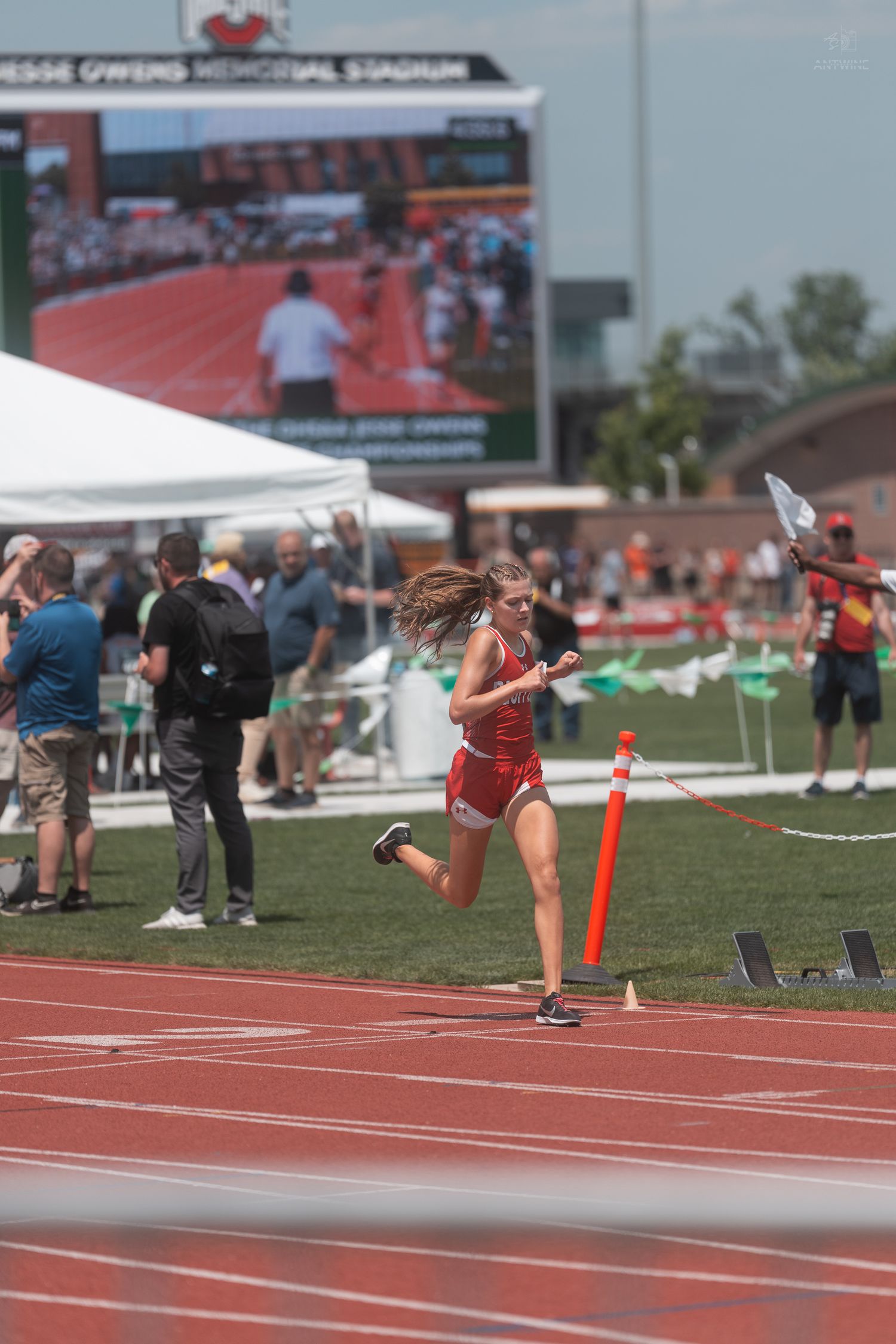 Female athlete in red uniform rounds a turn on the track at Jesse Owens Memorial Stadium during a championship meet.