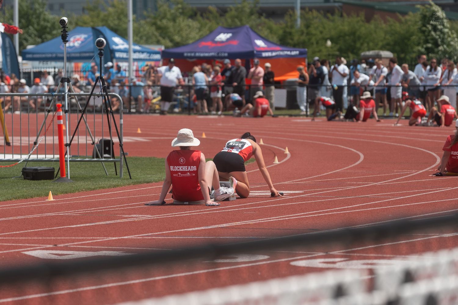 Two track athletes in starting blocks on red track at outdoor collegiate track and field competition.
