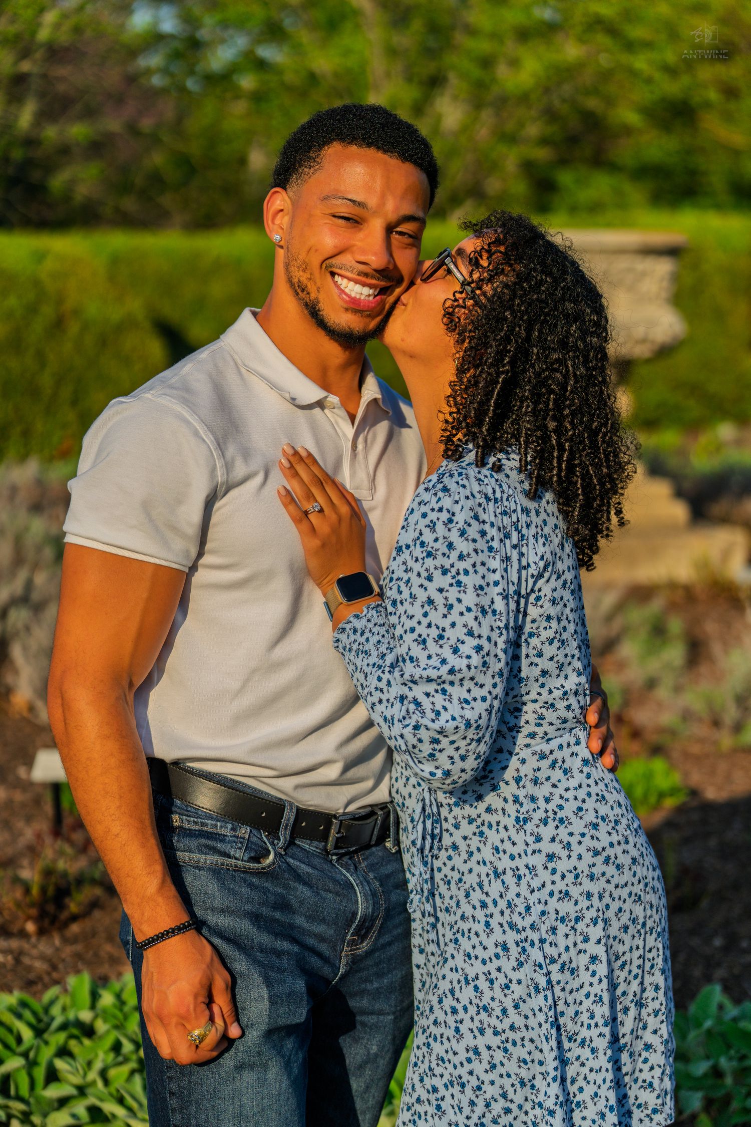 A happy couple shares a romantic moment outdoors, woman kissing mans cheek as he smiles in golden light.