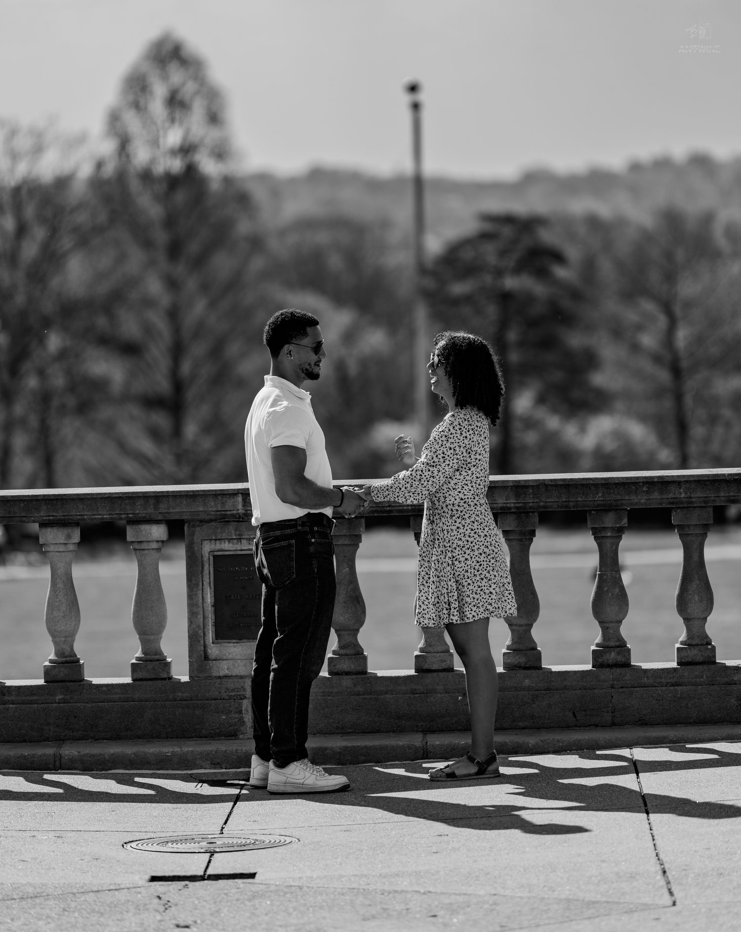Black and white romantic photo of couple holding hands on an ornate stone balustrade outdoors.