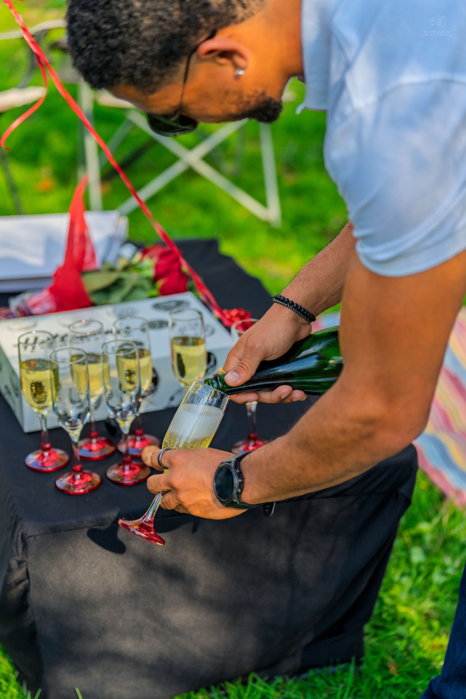 Man carefully pouring champagne into crystal flute glass at decorated outdoor garden celebration.