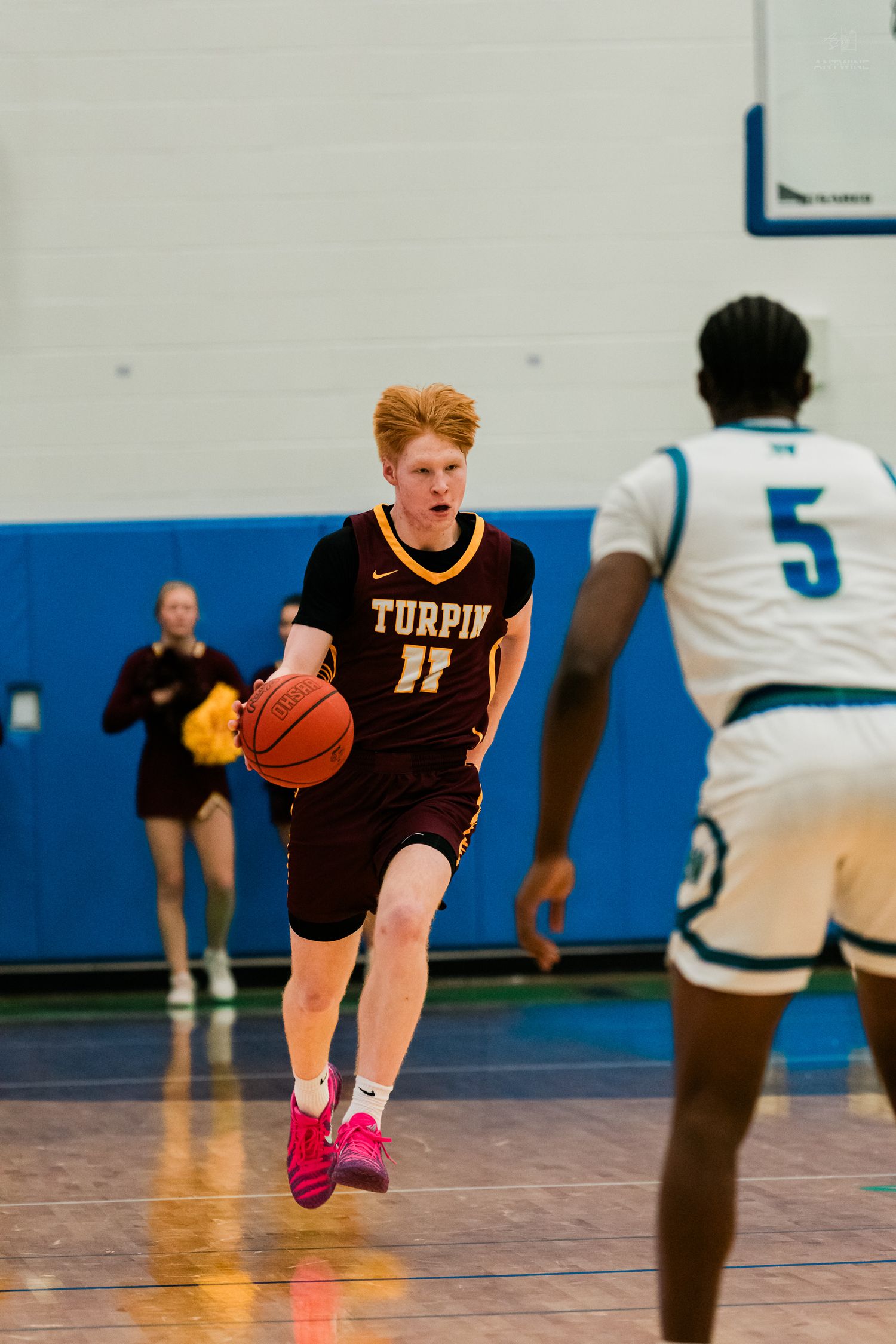 Turpin #11 red-haired player dribbles basketball past defender #5 in white during high school game.