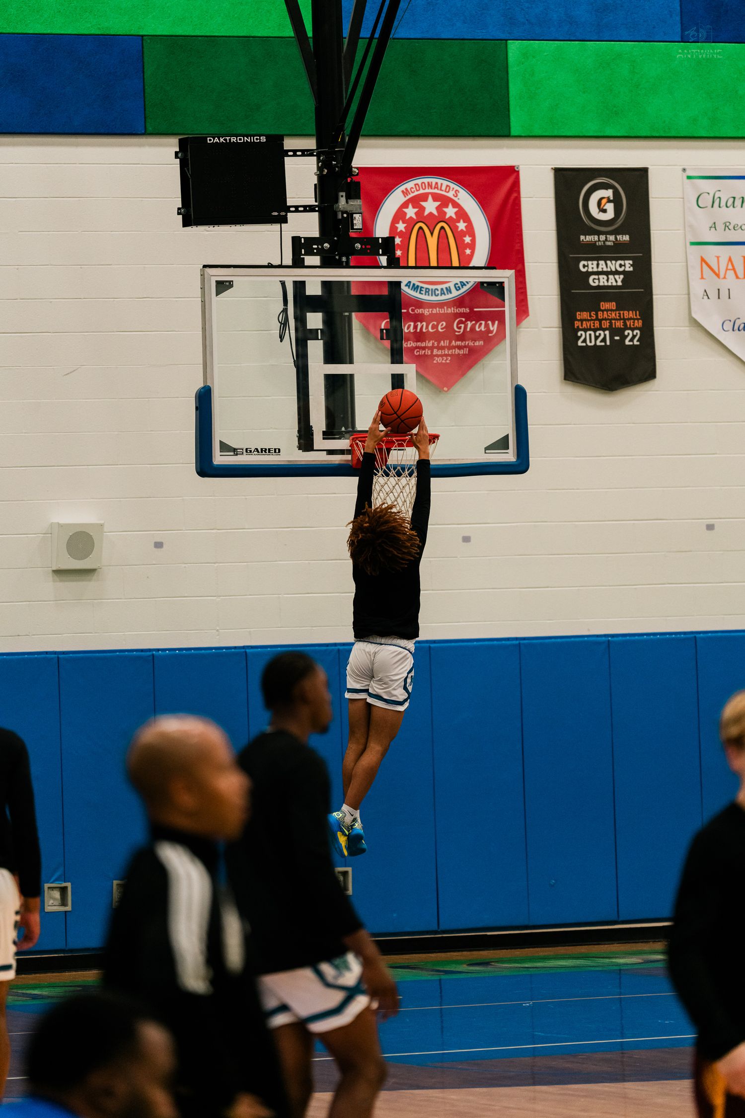 A basketball player dunks the ball during a game under a McDonald's All American banner in a gym.