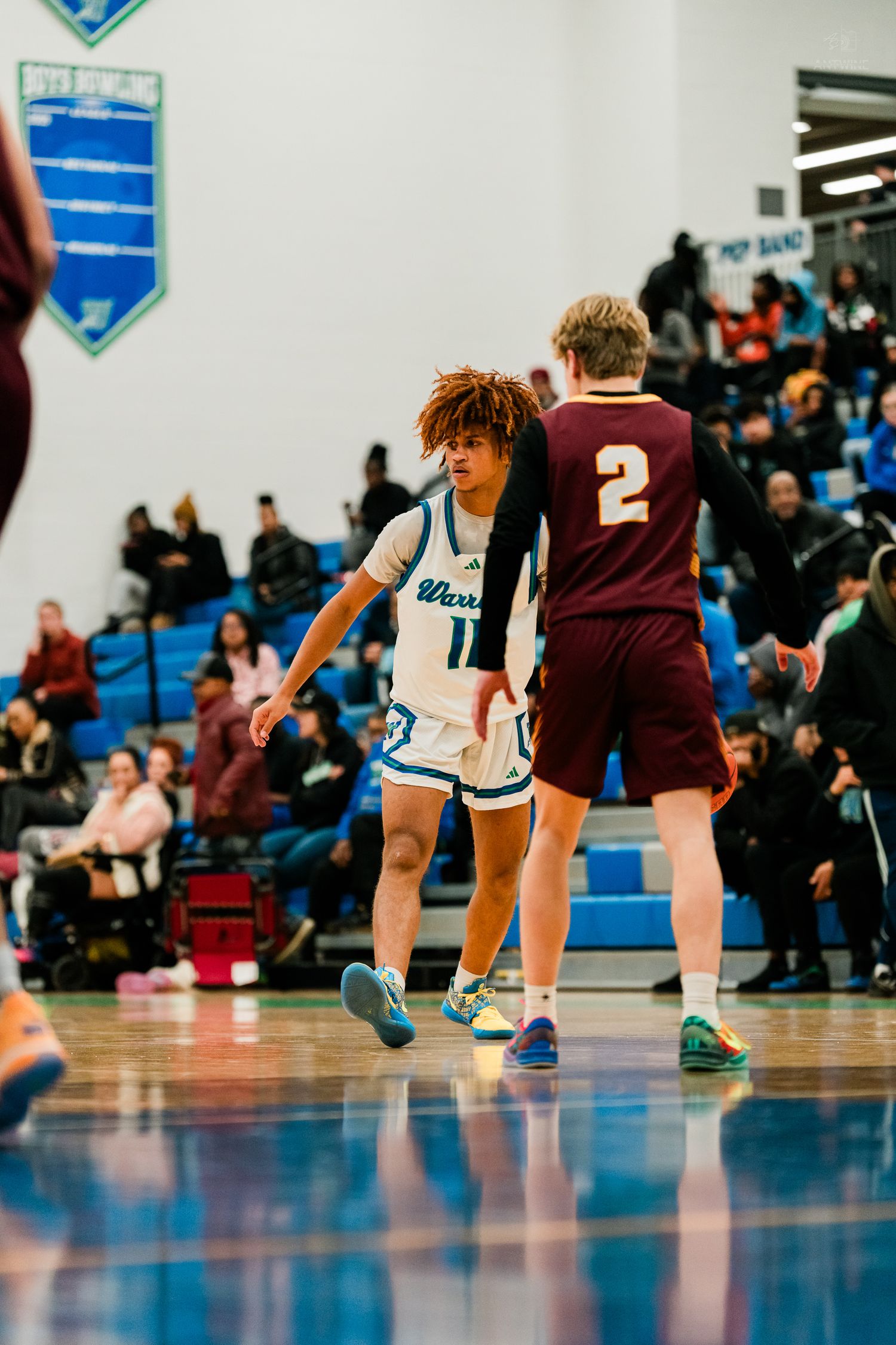 Warriors number 11 in teal uniform guards maroon-uniformed player number 2 on a high school basketball court.