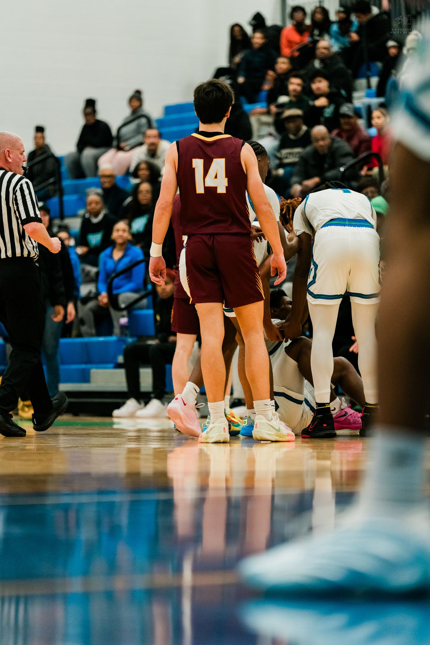 Turpin player number 14 stands near referee while home team players huddle during high school basketball game.