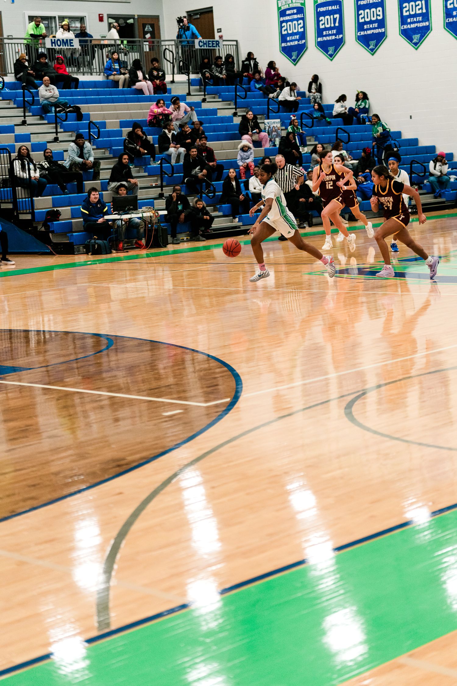High school girls basketball player in white dribbles upcourt against maroon Turpin defenders.