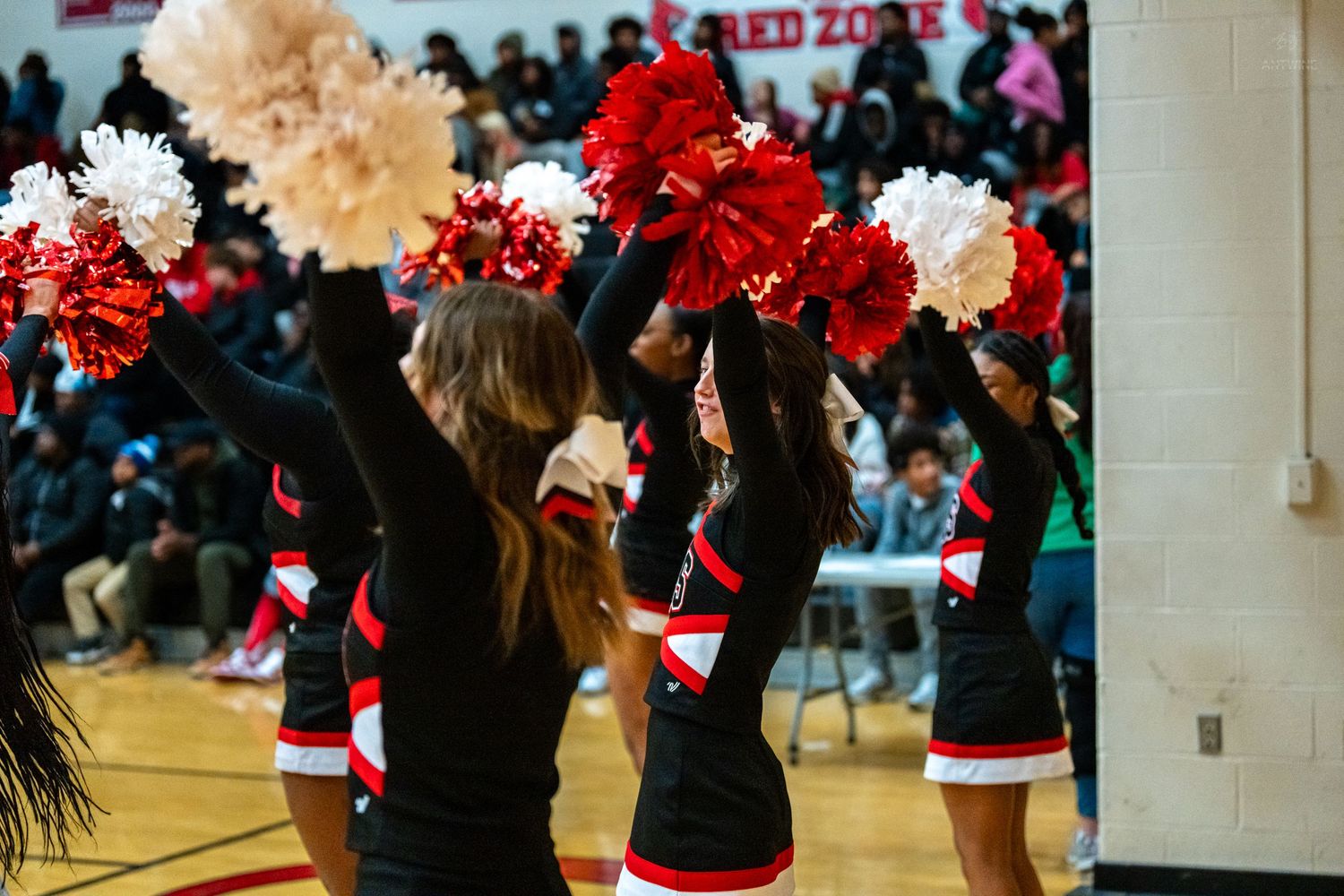 High school cheerleaders in black red and white uniforms perform with pom poms during basketball game.