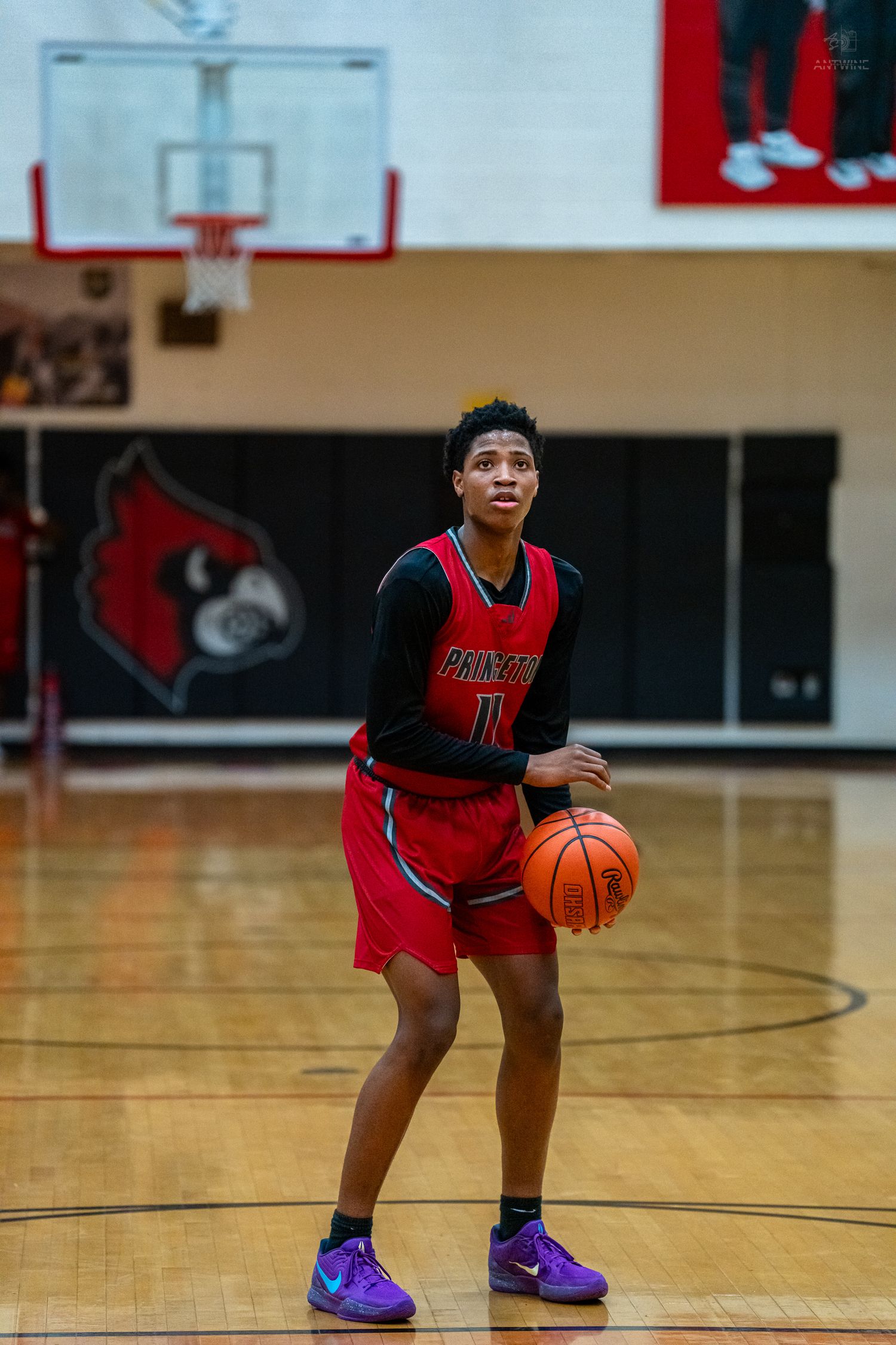 High school basketball player in red uniform holds ball on court in front of Cardinals logo.
