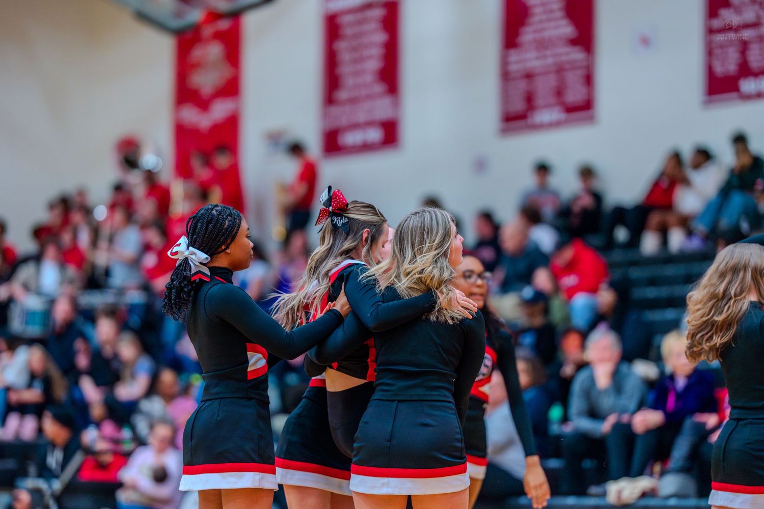 High school cheerleaders in black and red CARDS uniforms huddle together during a basketball game.