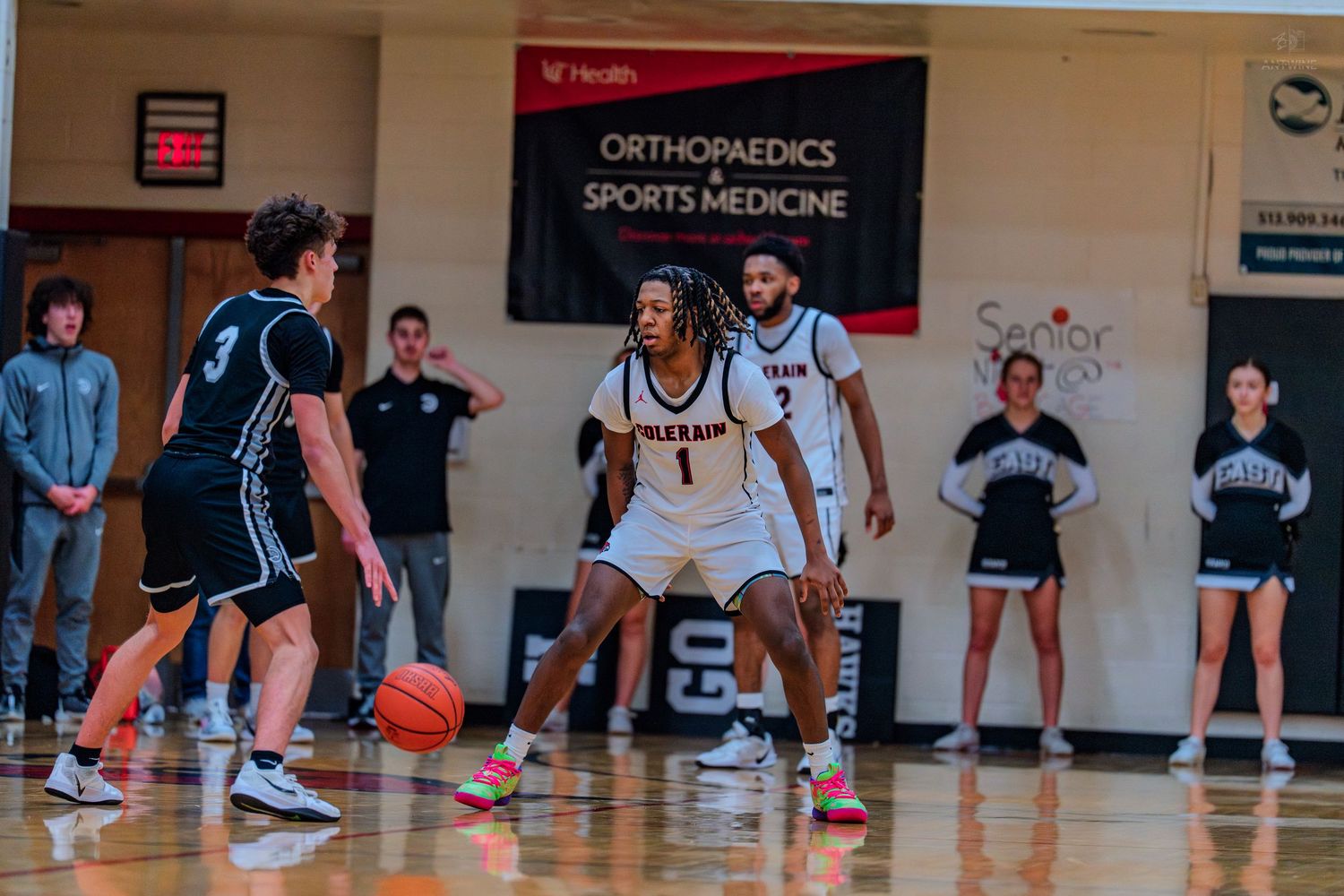 Colerain basketball player #1 plays defense against opponent near sports medicine banner.
