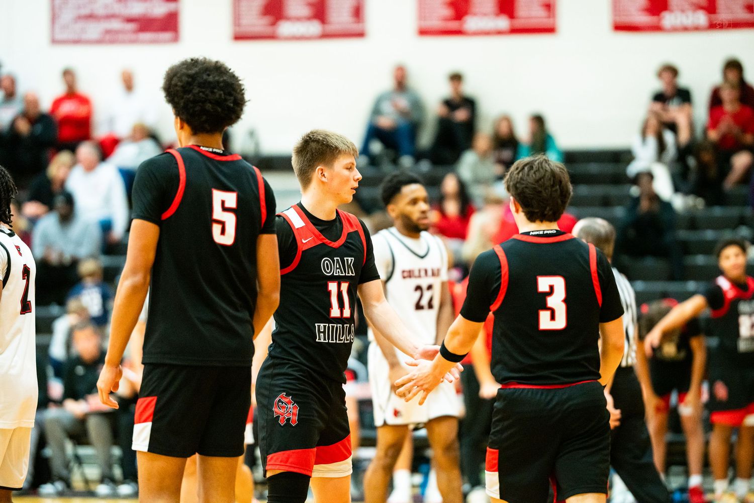 Three basketball players in black uniforms huddle together on the court during a high school game.