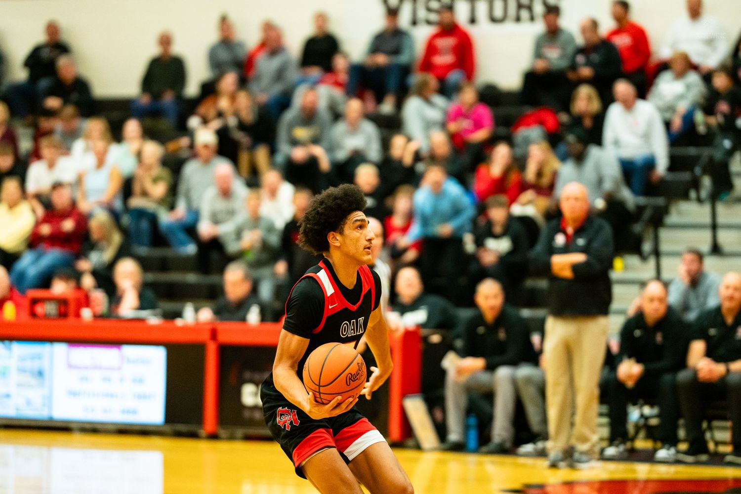 High school basketball player dribbles ball during game with packed crowd in gymnasium.