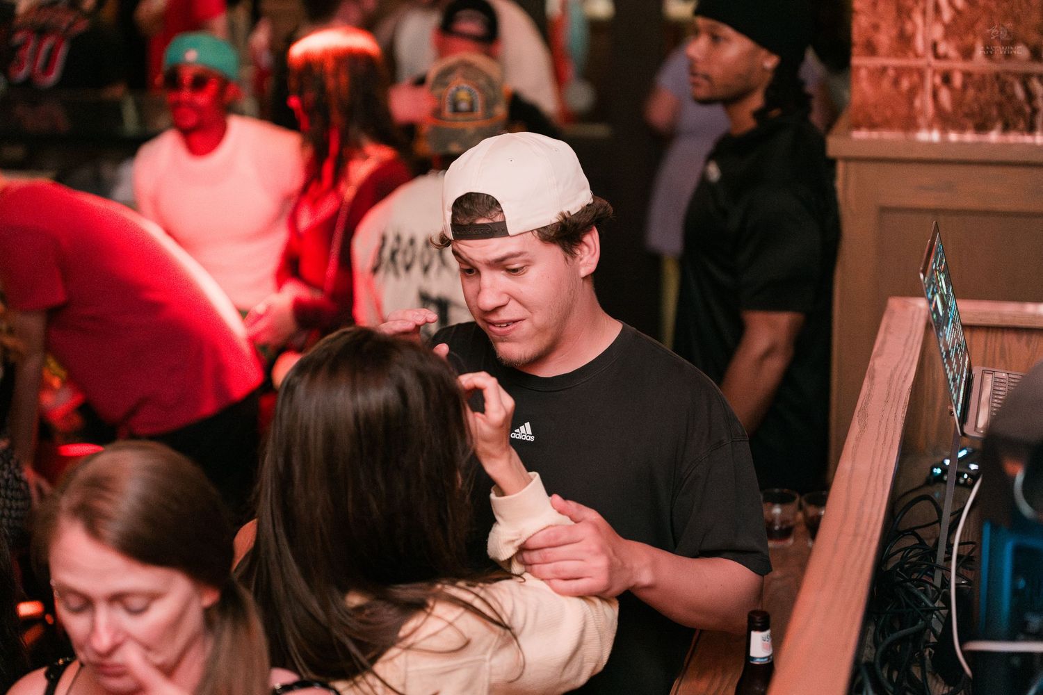 Young man in backwards cap dancing closely with a woman at a busy nightlife venue.