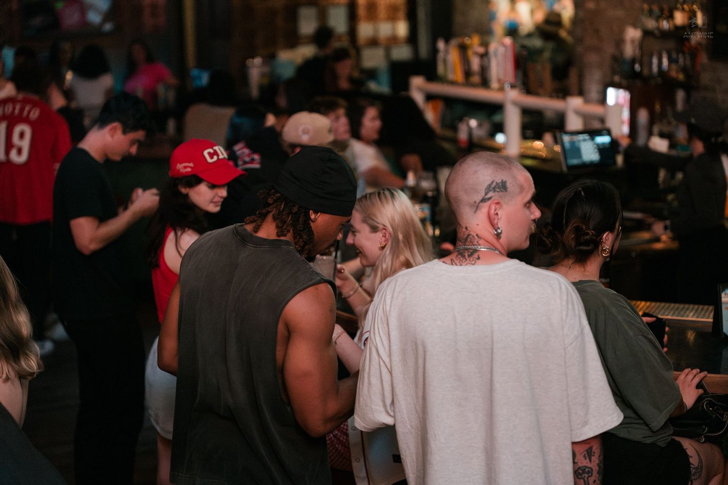 Diverse group of people socialize at a bar counter in a lively nightclub setting.