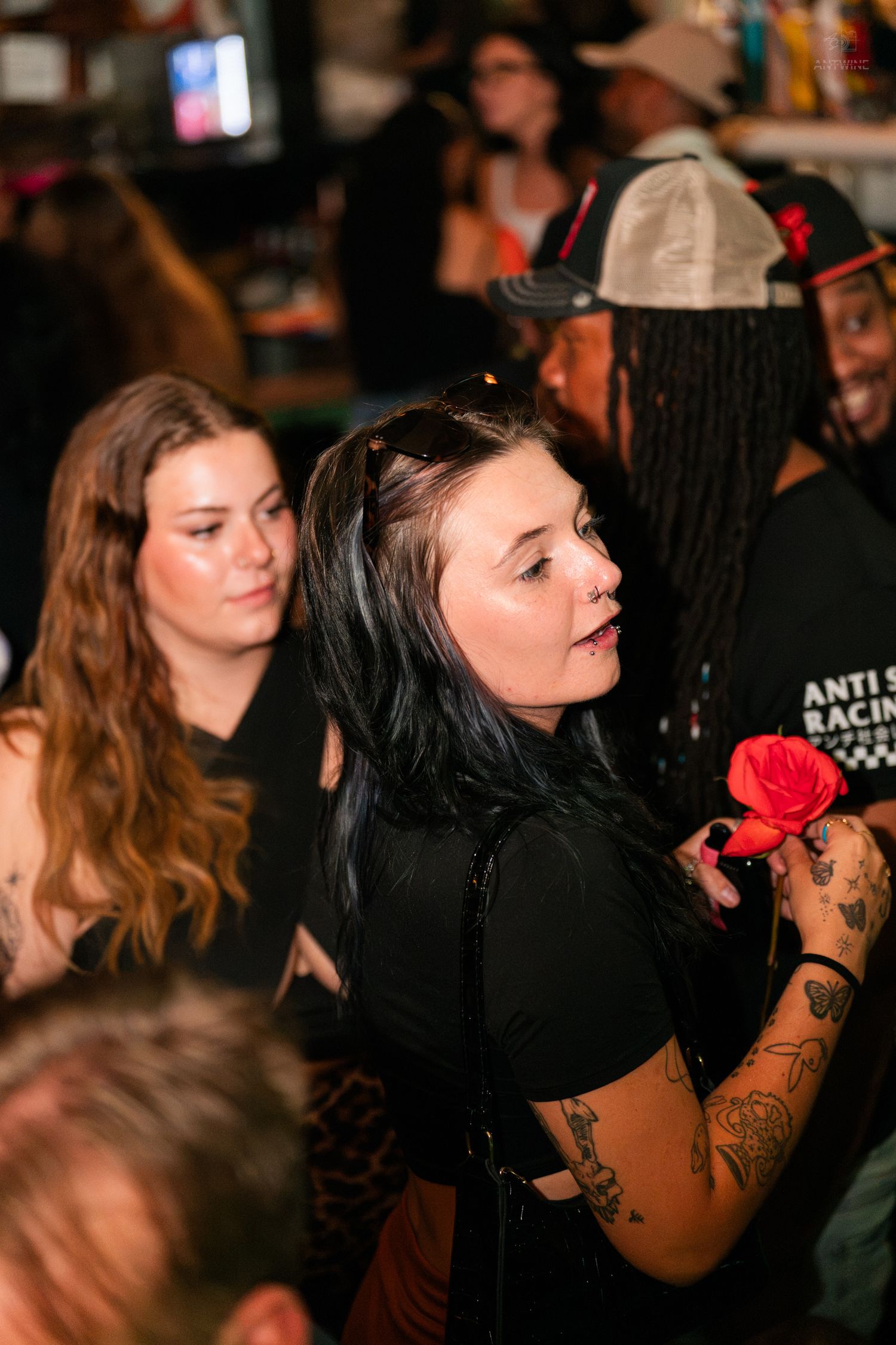 Tattooed woman holding a red rose while socializing at a nightclub event.