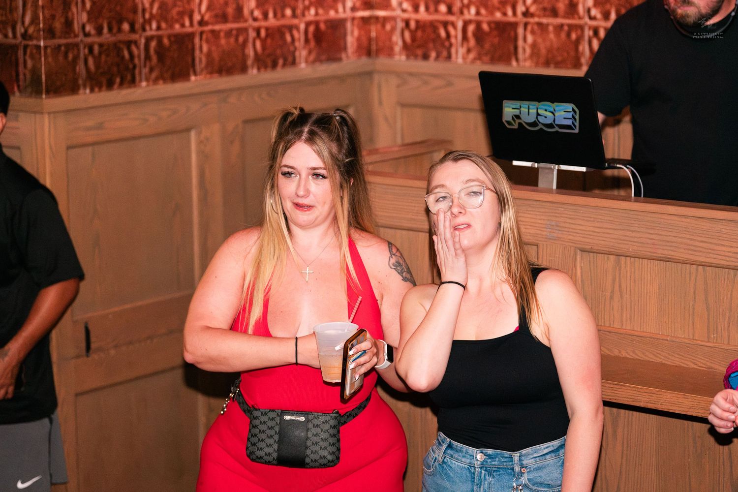 Two blonde women posing together near a DJ booth at an indoor bar event.
