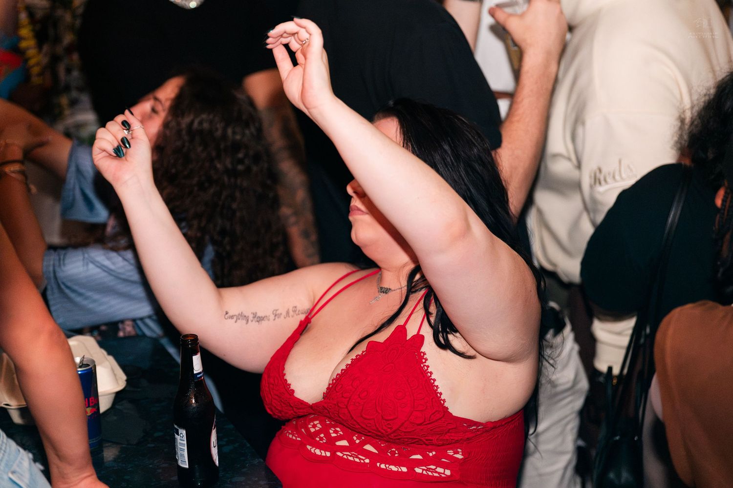 Woman in red top dancing with arms raised at a lively nightclub party event.