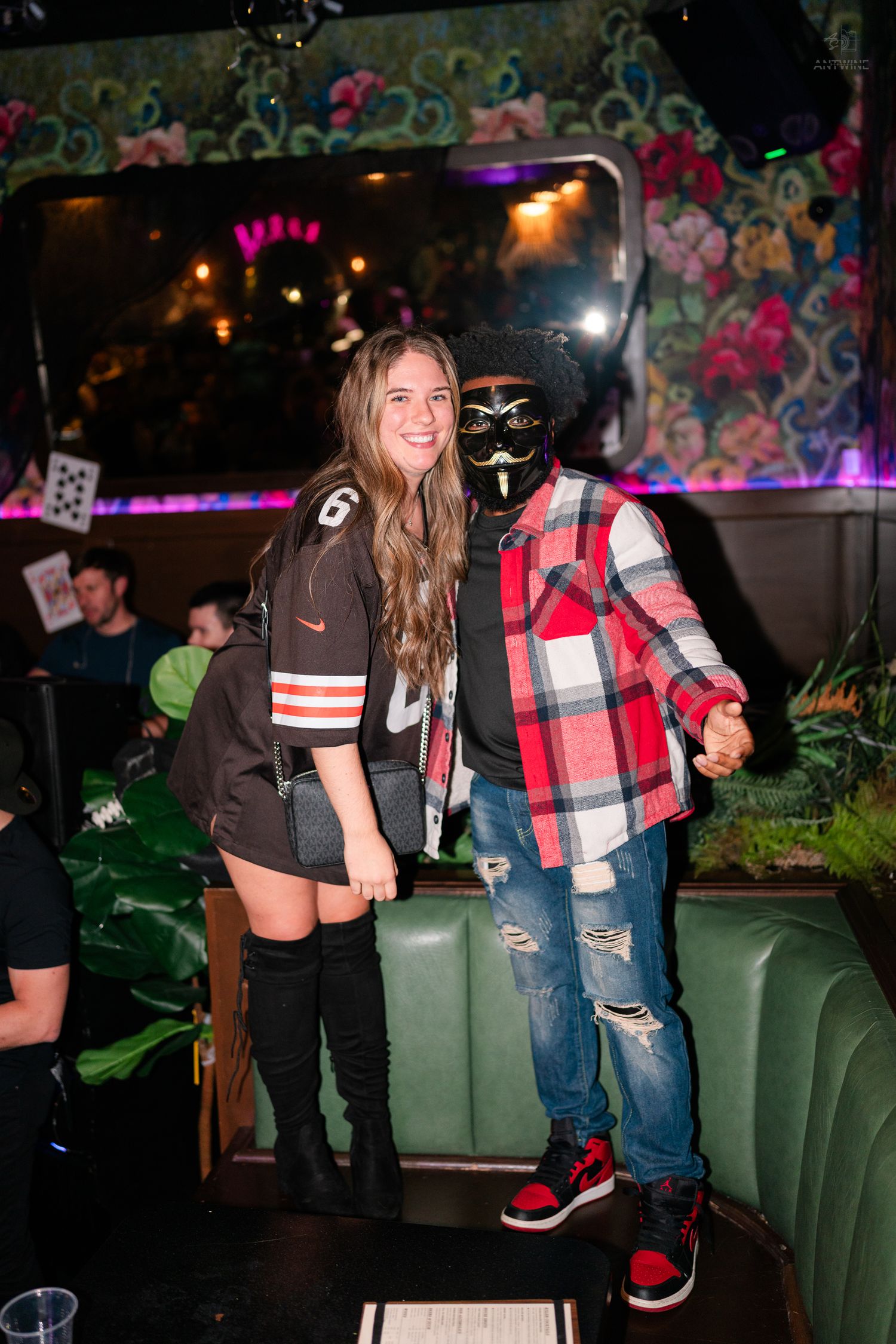 Couple posing at a Halloween party, woman in jersey costume and man wearing a Guy Fawkes mask.