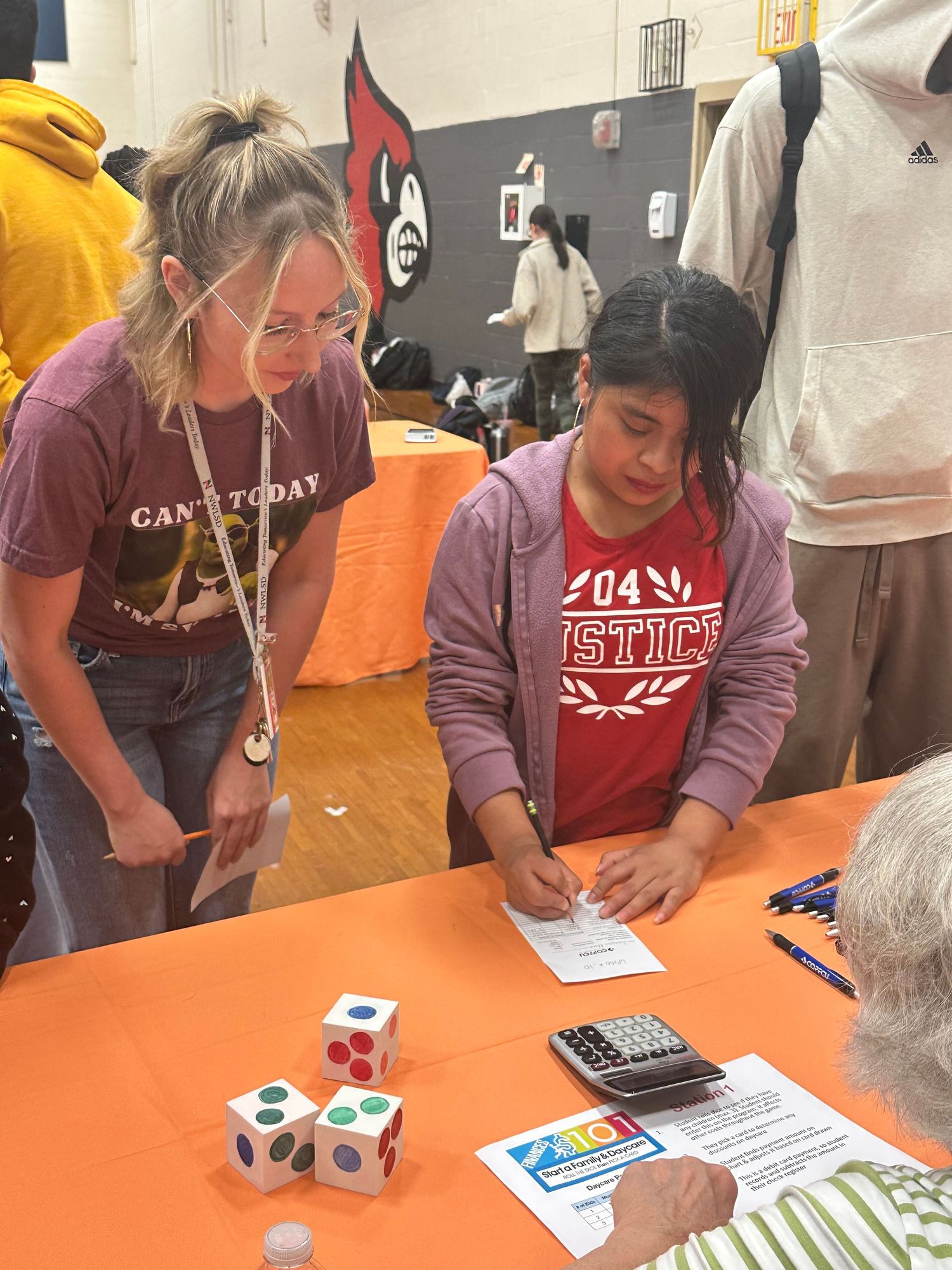 Two students collaborate on a math activity with oversized dice at an educational fair in a school gymnasium.