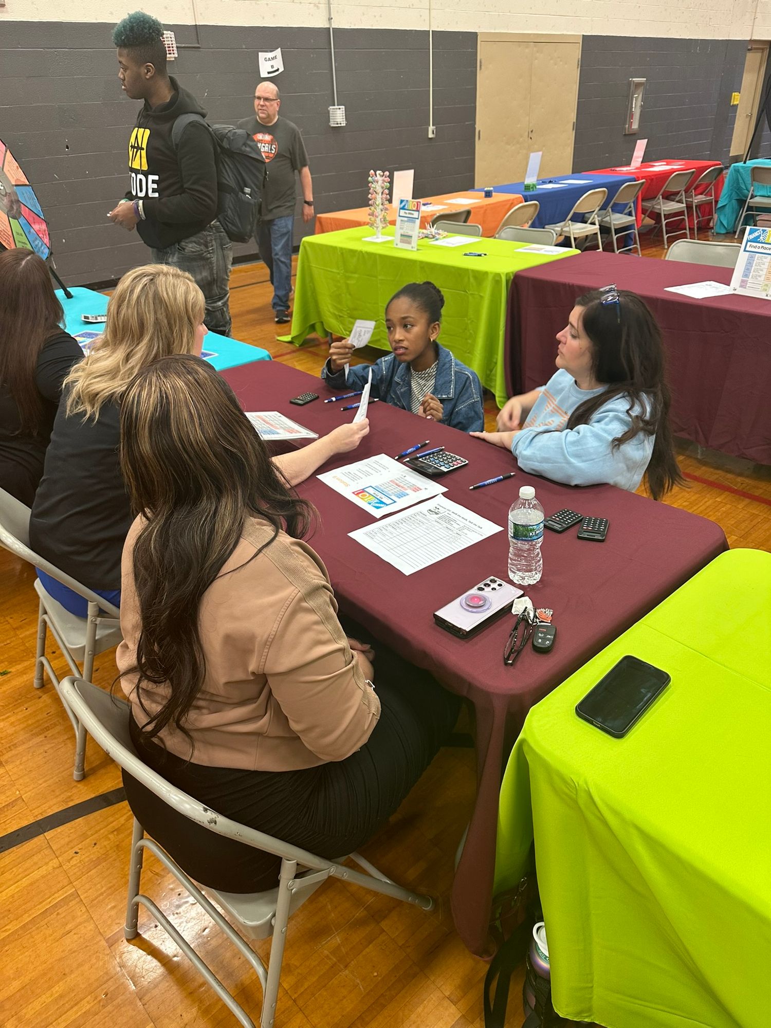 Students meet with recruiters at colorful tables during a school job fair event in a gymnasium.