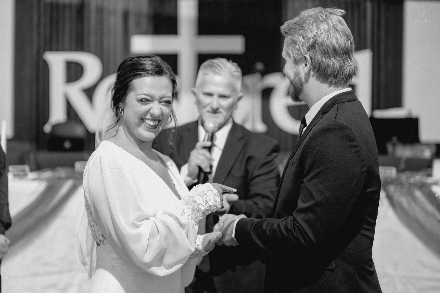 Bride and groom exchange vows at wedding ceremony in black and white photo with officiant behind them.