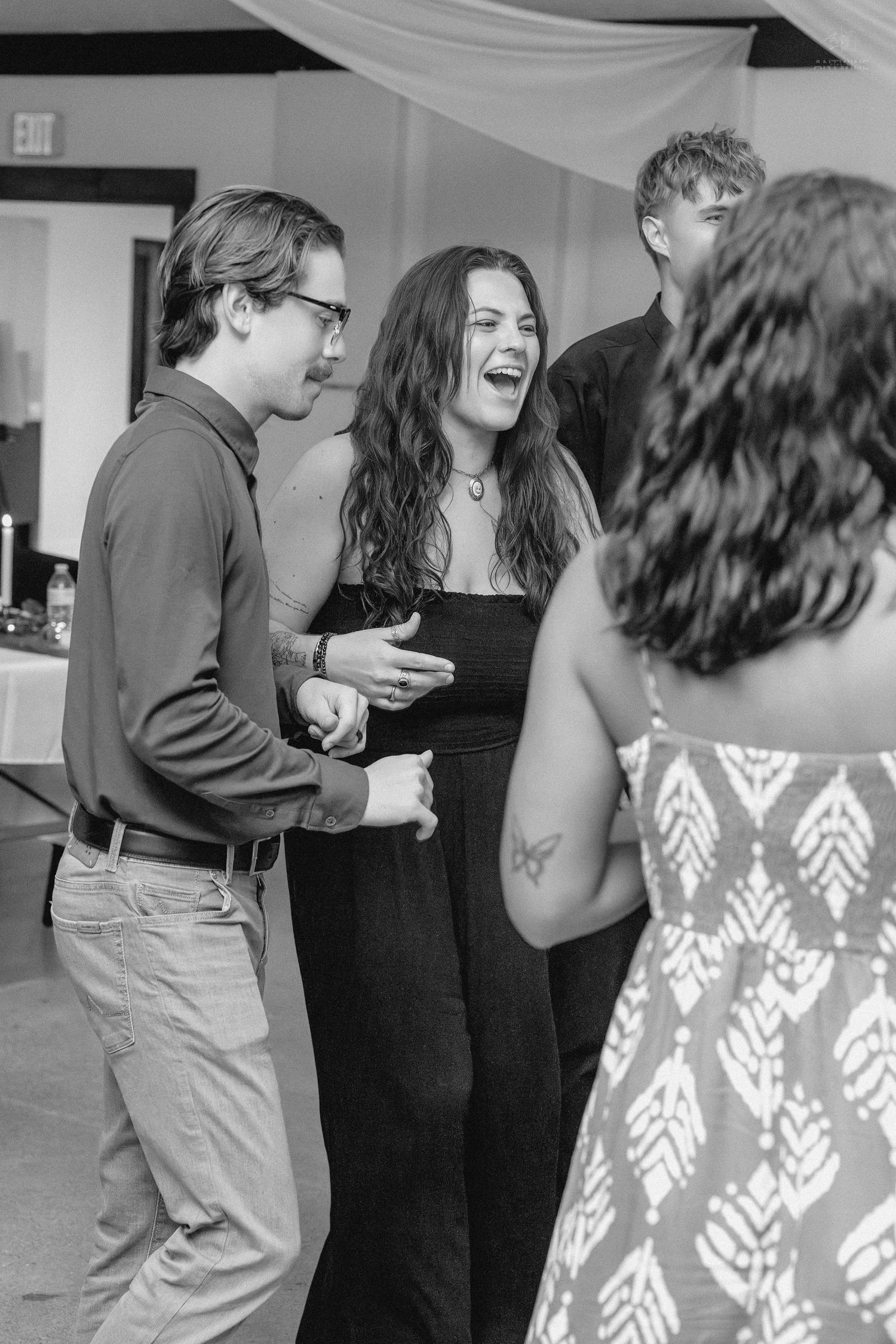 Black and white photo of guests laughing and dancing together at a wedding reception.