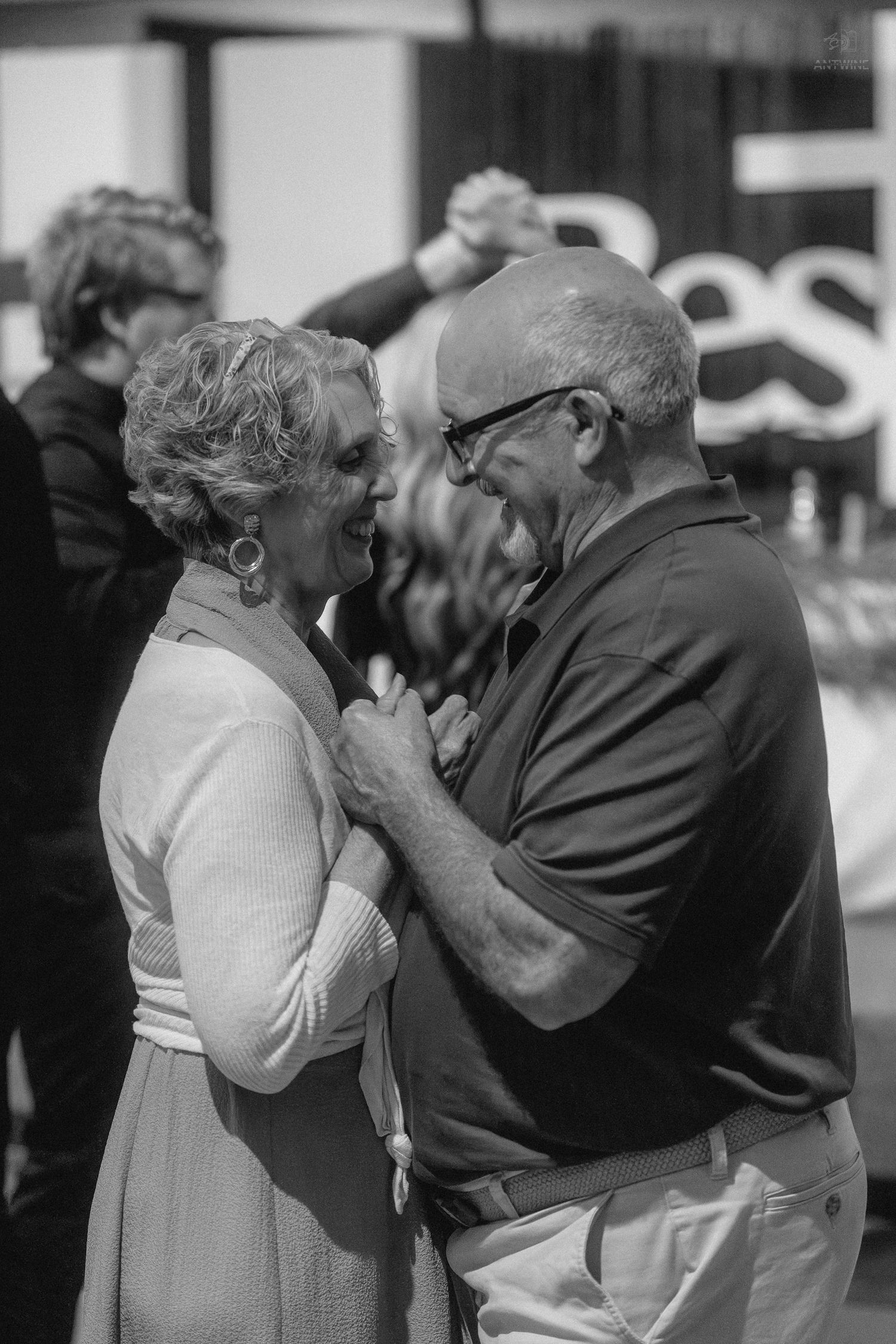 Elderly couple sharing a tender dance together outdoors in a black and white candid photo.