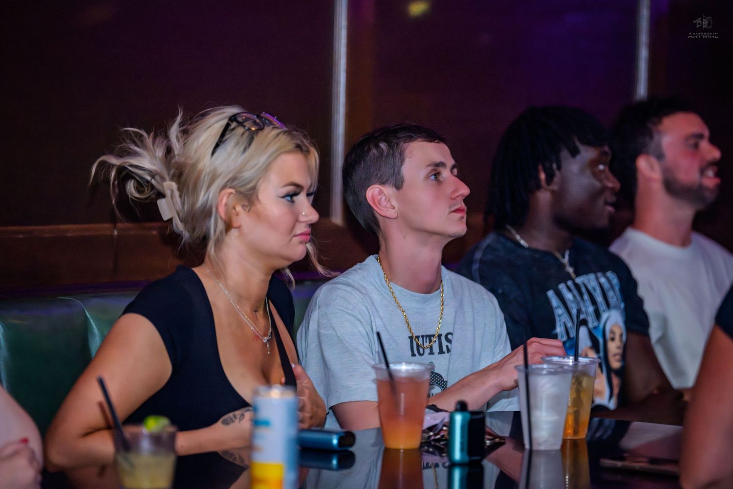 Group of friends sitting at a bar enjoying drinks under colorful lighting.