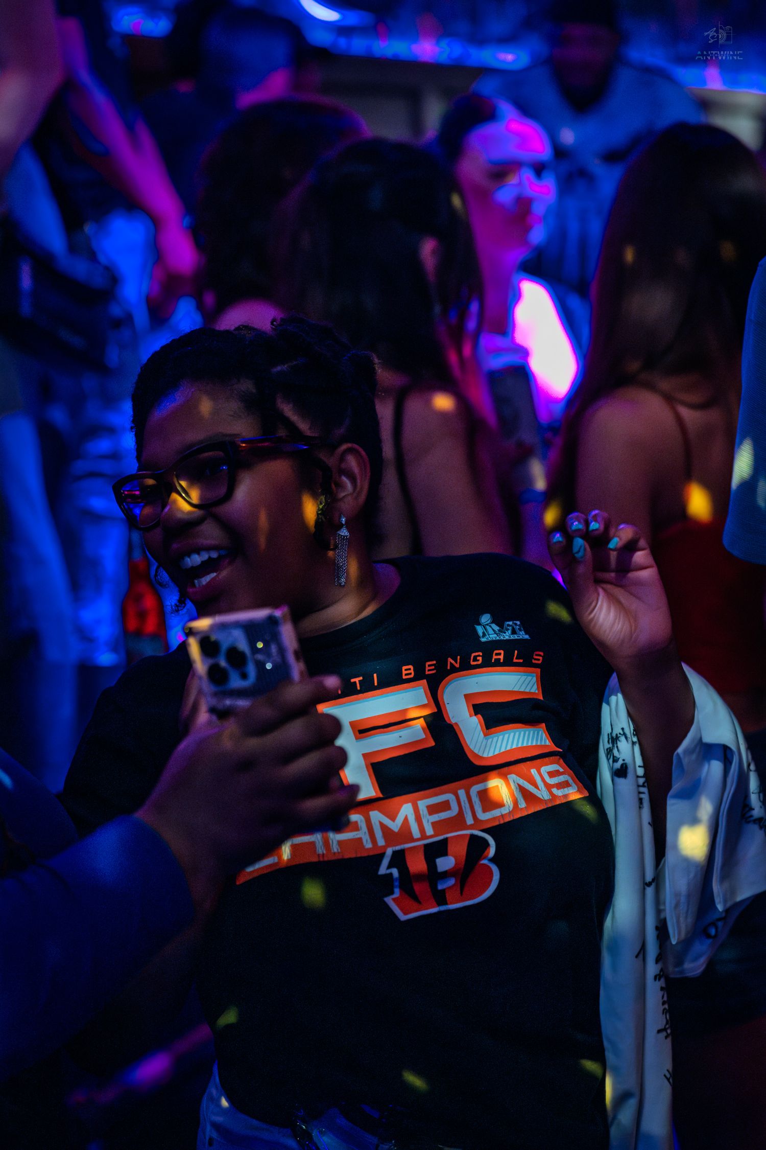Woman in Bengals AFC Champions shirt dancing and smiling at a lively neon-lit nightclub event.