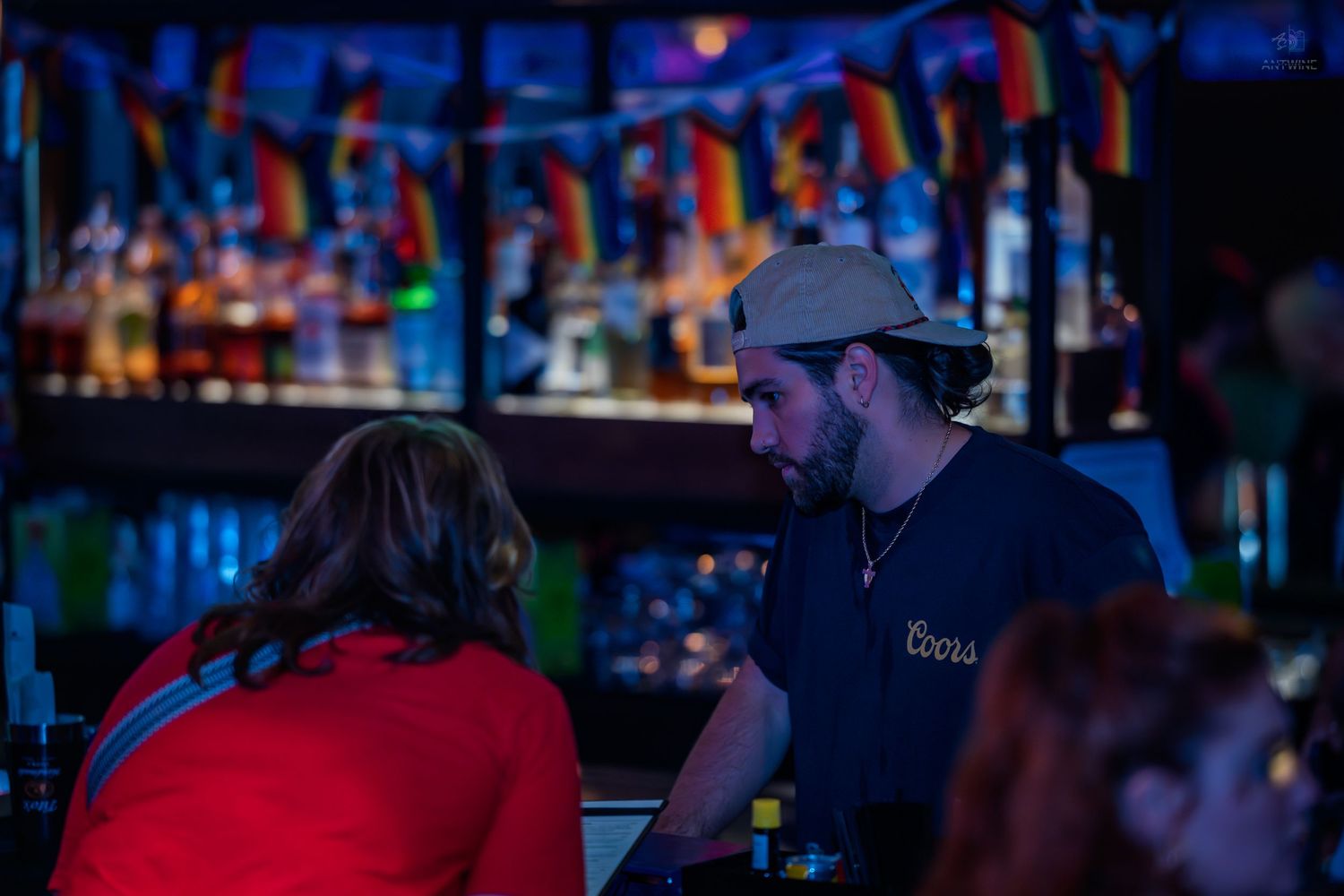 Bartender in cap serving a customer at a colorful bar decorated with German flags.