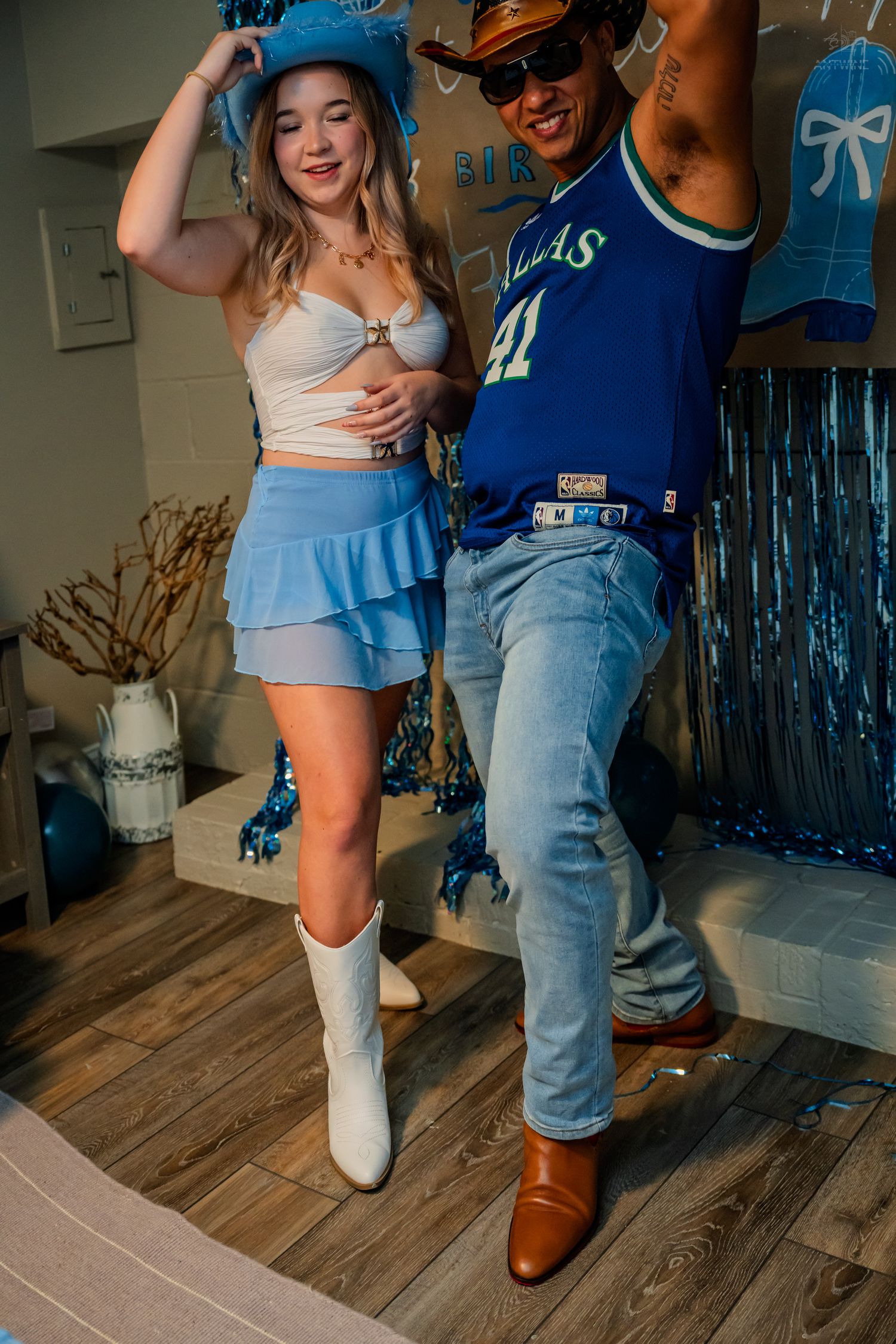 Two friends dancing at a blue-themed 21st birthday party, wearing cowboy hats, boots, and a Dallas jersey.