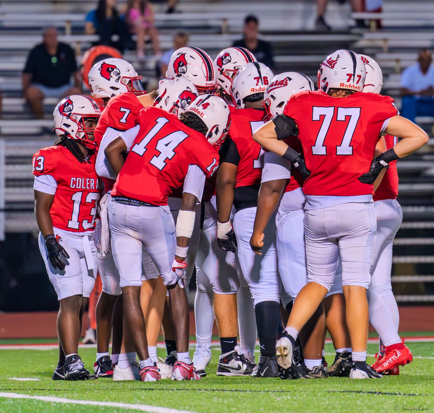 Colerain football team huddles together on the field wearing red uniforms during a game.