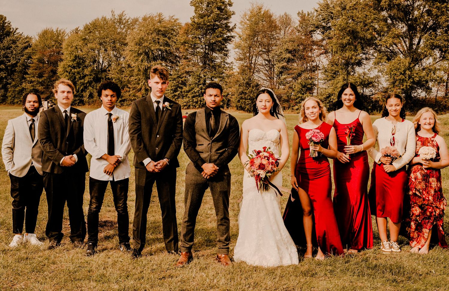 Wedding party posing outdoors, groomsmen in suits and bridesmaids in red dresses.
