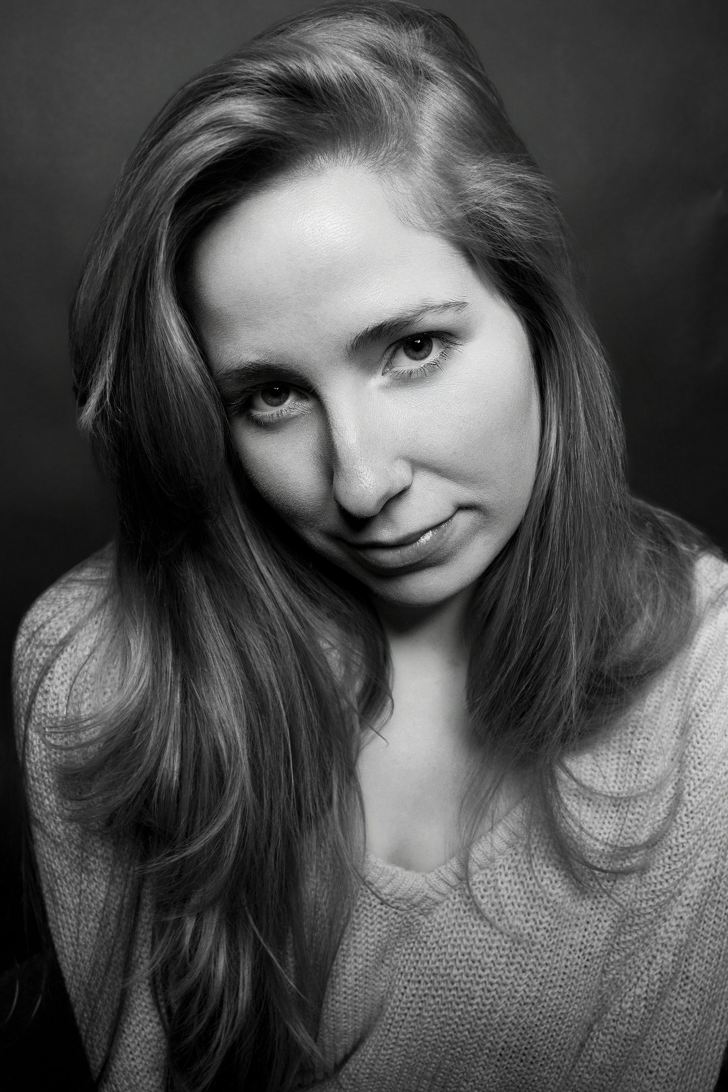 Black and white studio portrait of a woman with long hair in a knit sweater, slight smile.
