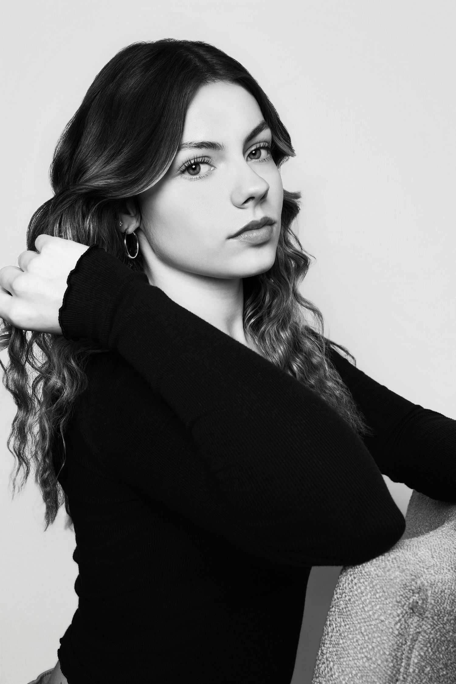 Black and white portrait of a young woman with long wavy hair in a black top, posing confidently.