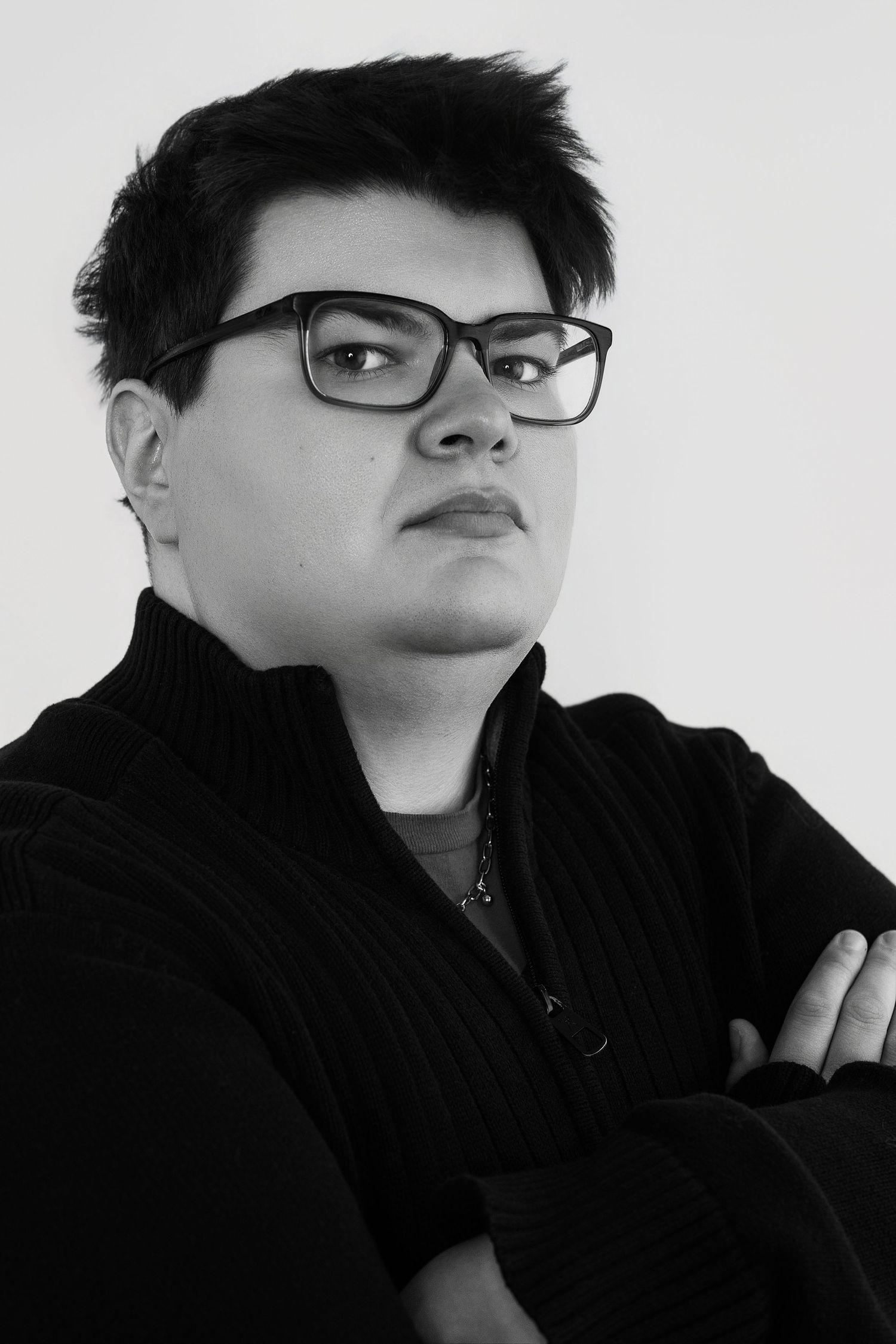 Black and white portrait of a young person in glasses and black turtleneck with arms crossed.