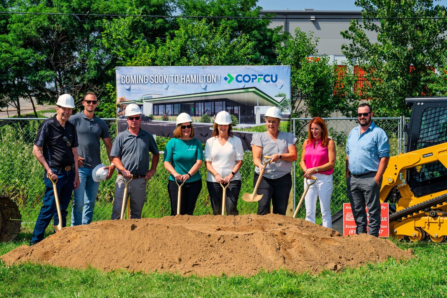 Group of eight people in hard hats holding shovels at COPFCU Hamilton groundbreaking ceremony outdoors.