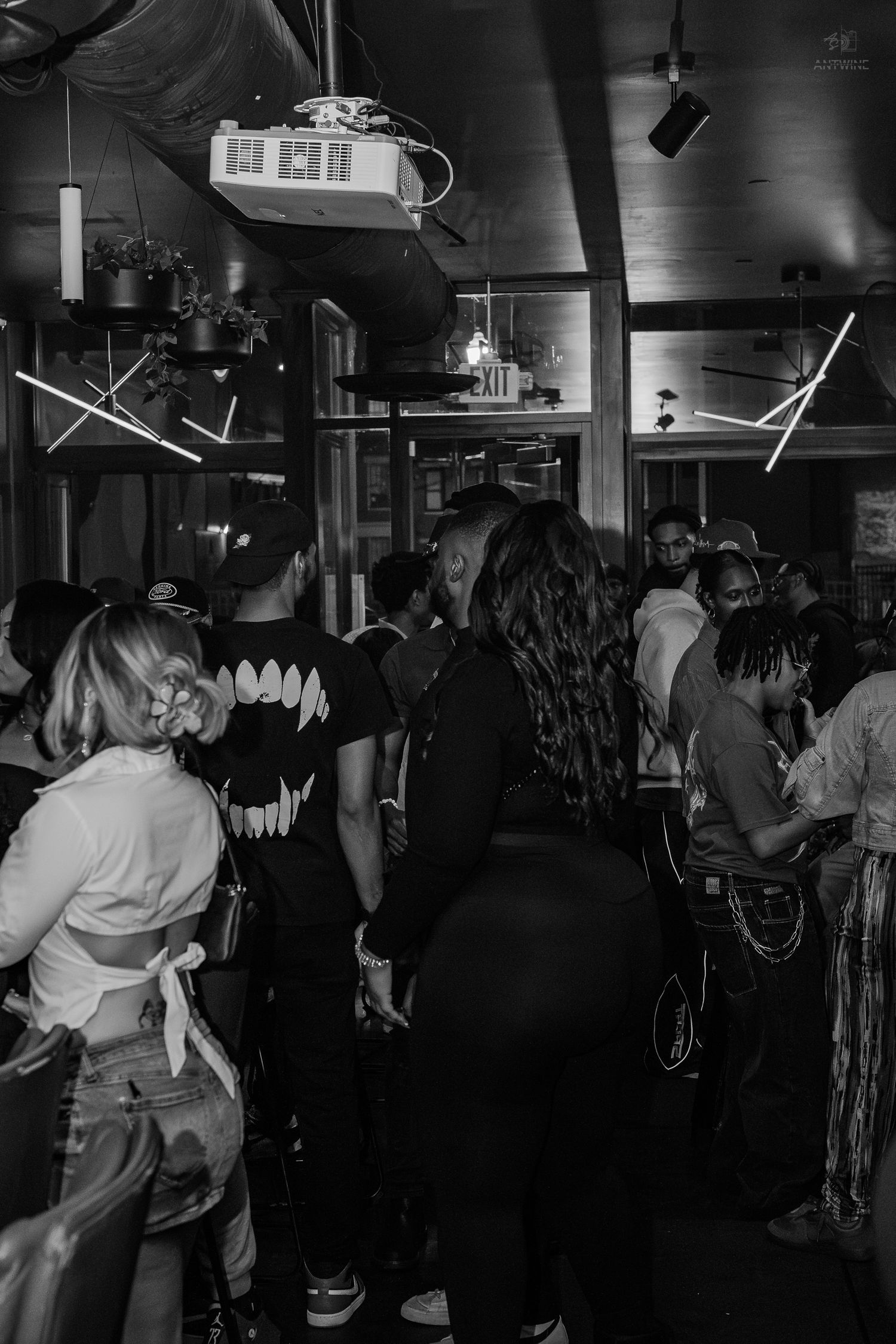 Black and white photo of a crowded indoor party with people socializing under neon lights.