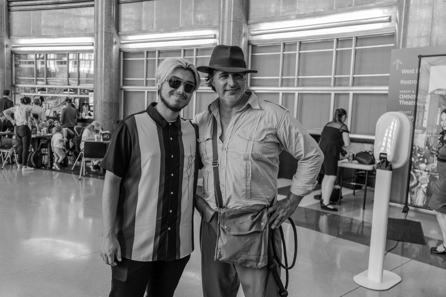 Two men posing together indoors at a busy event venue in a black and white photo.
