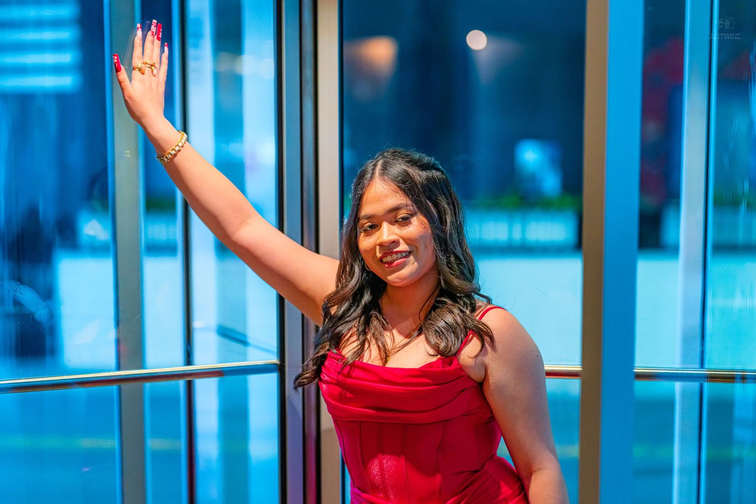 Young woman in red dress posing elegantly by glass doors in urban setting at night.