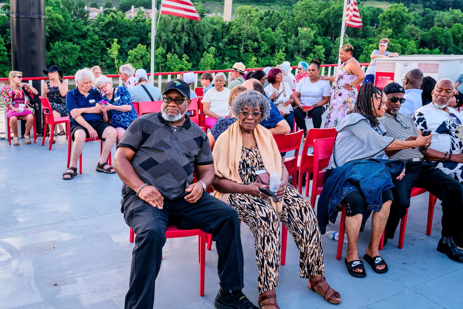 Diverse group of people seated in red chairs at outdoor evening community gathering.