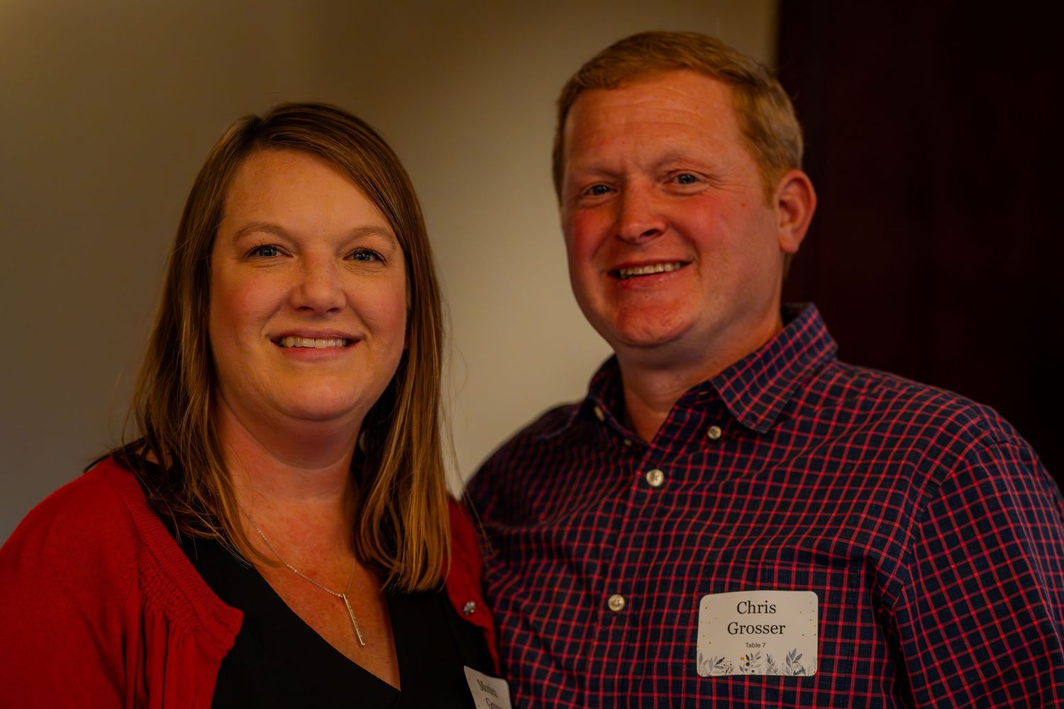 Smiling couple posing together at an event, man wearing plaid shirt with name tag reading Chris Grosner.