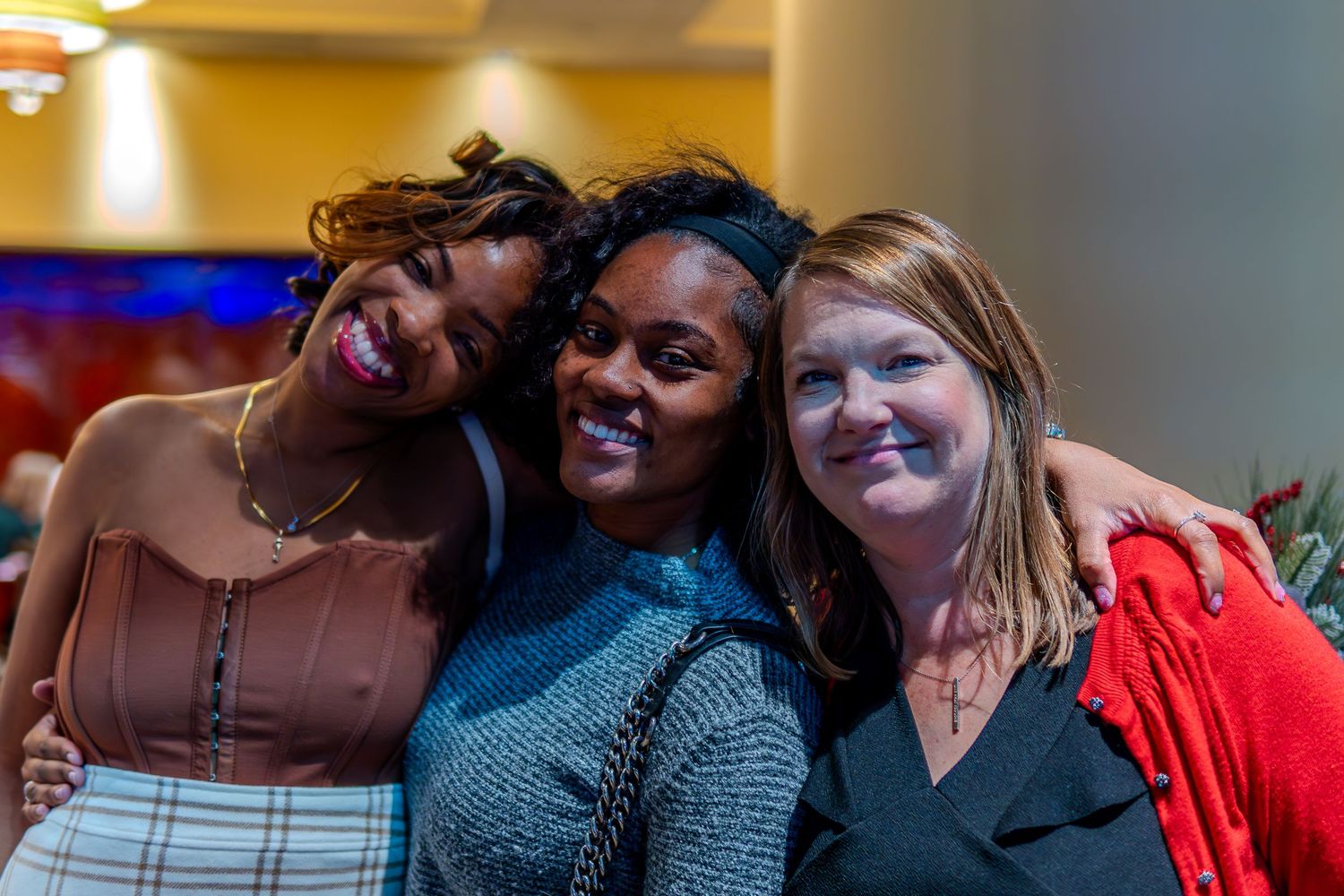 Three smiling women posing together for a photo at an indoor social event.