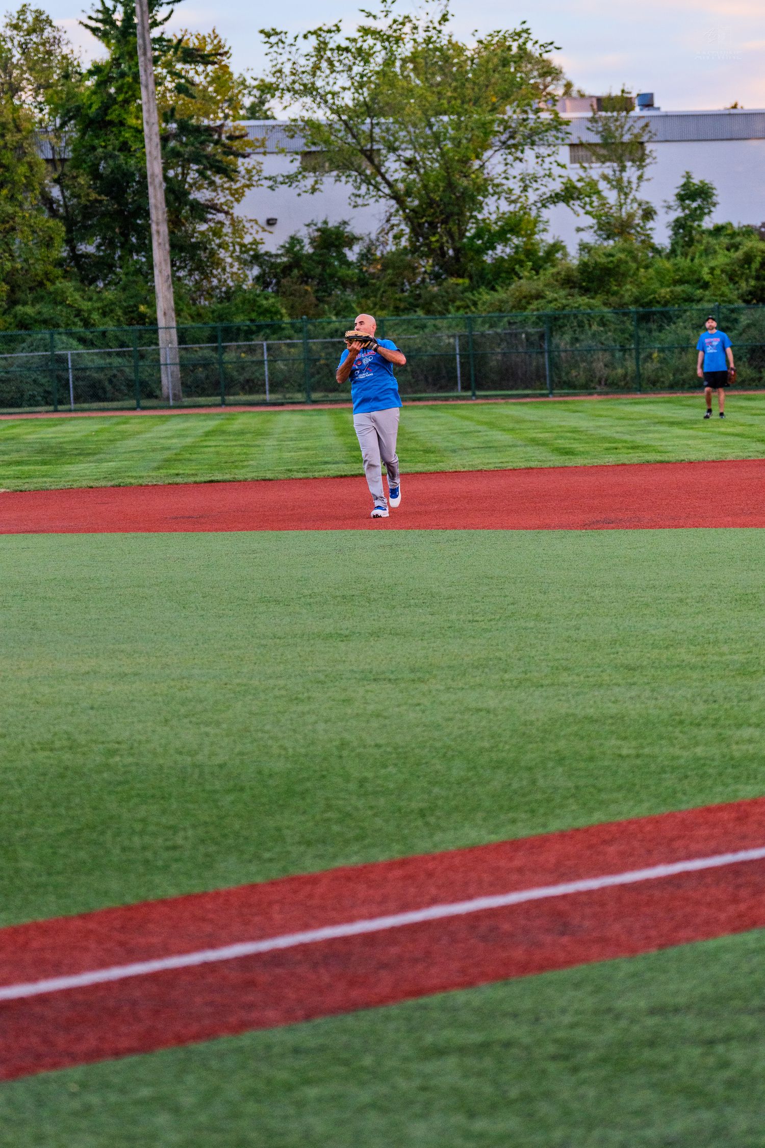 Player in blue jersey fields ball in outfield during evening recreational softball game.