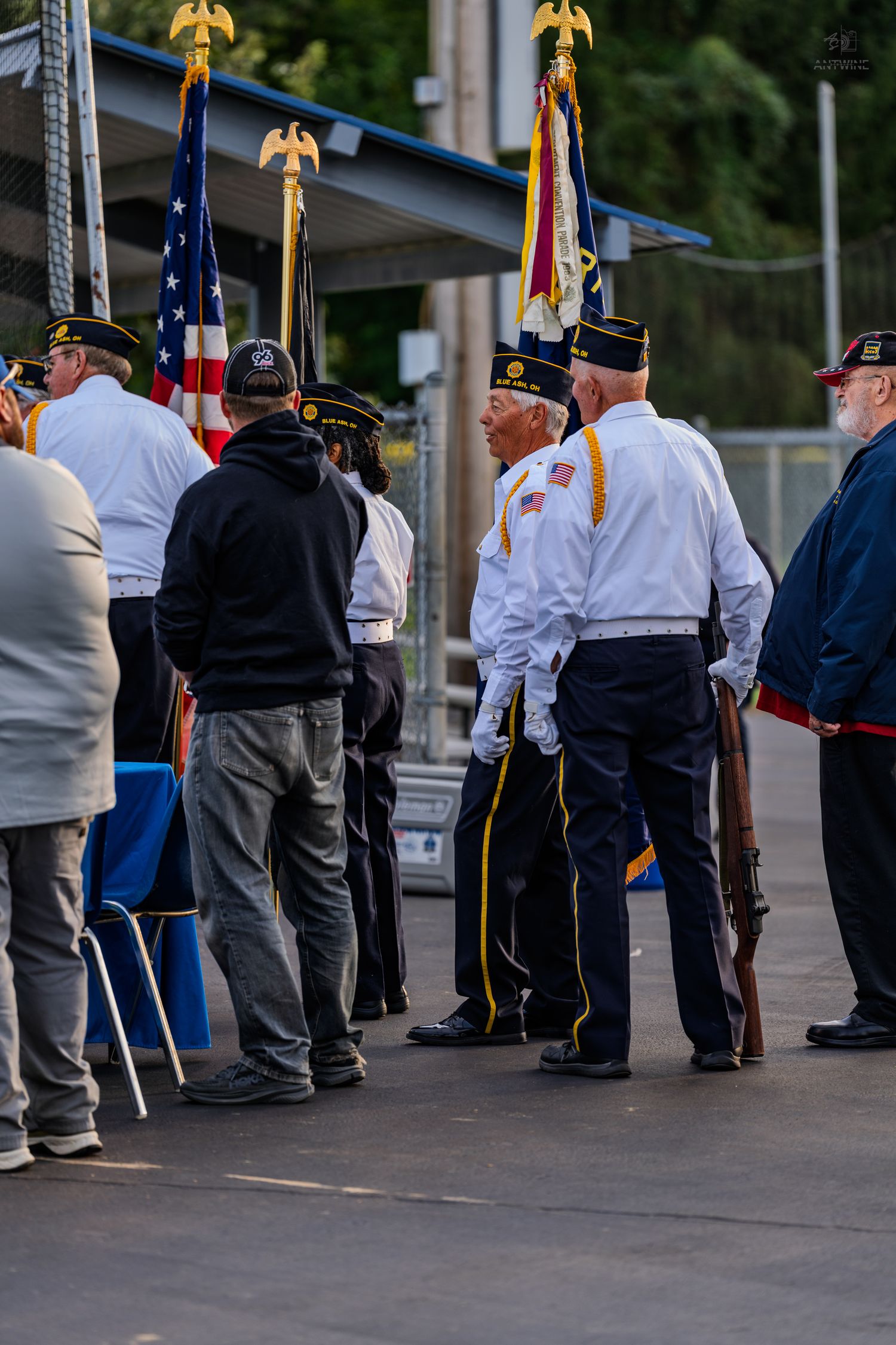 Veterans in uniform with rifles and American flags at a military color guard ceremony outdoors.